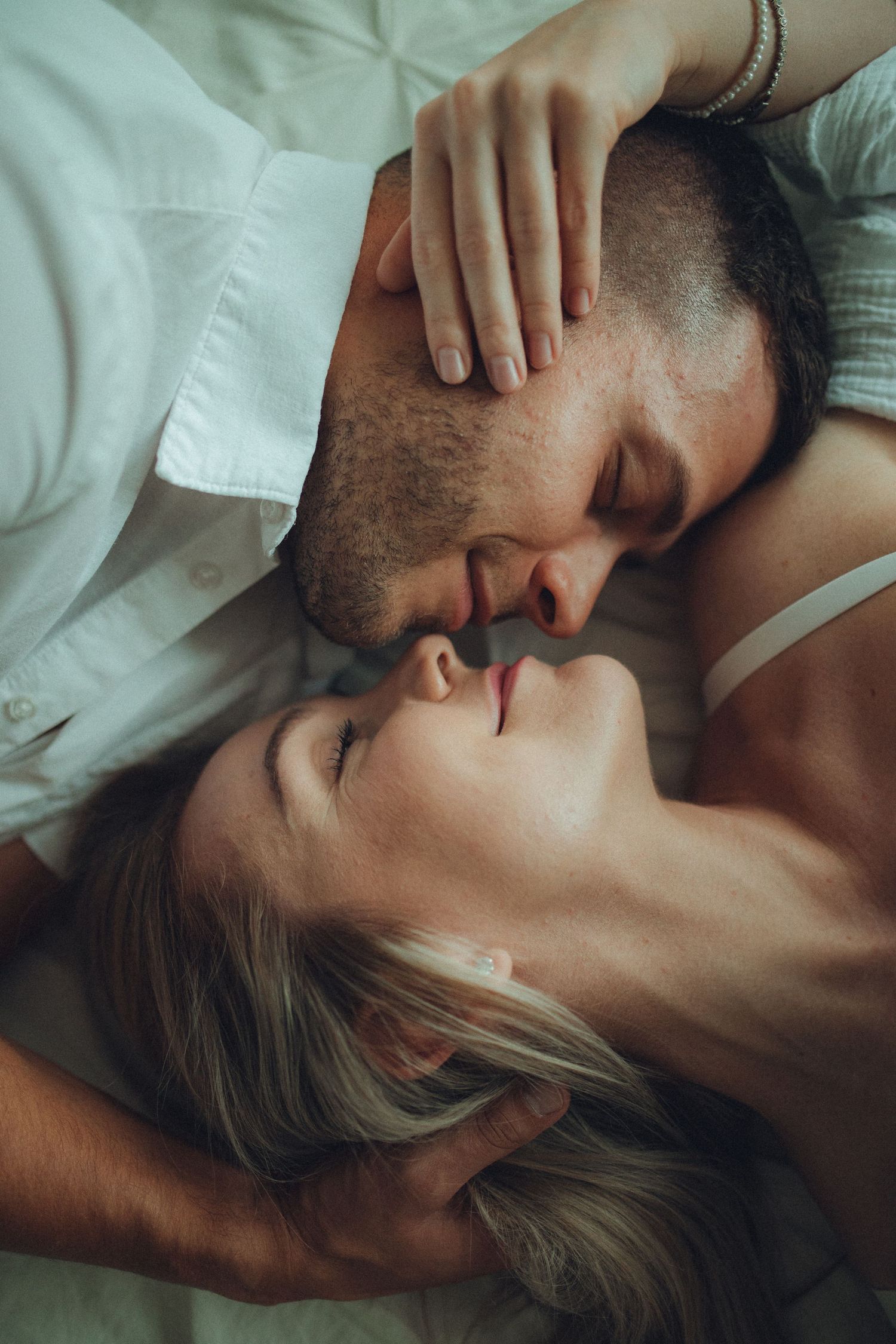 An intimate moment between a couple lying close together on white bedding.