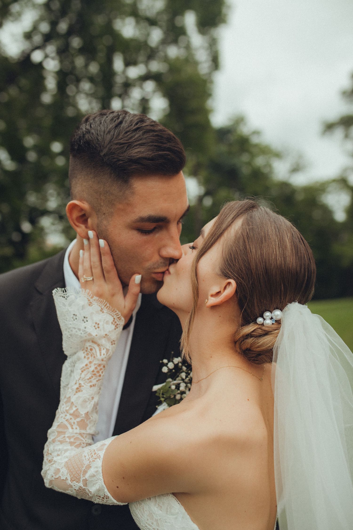 Intimate wedding couple sharing a tender kiss outdoors with bride in lace detailed gown.