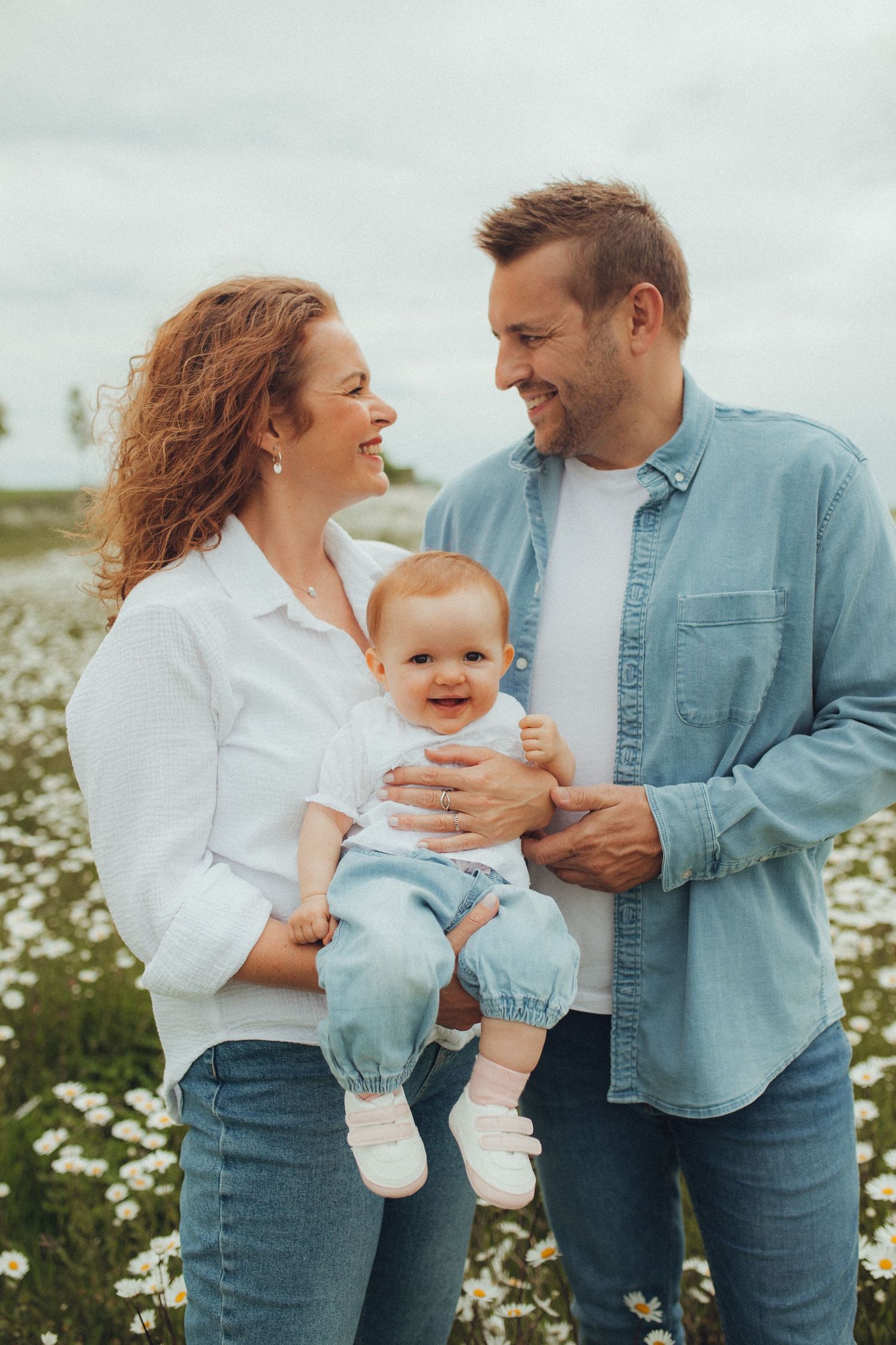 Happy family moment in blooming daisy field on cloudy day.