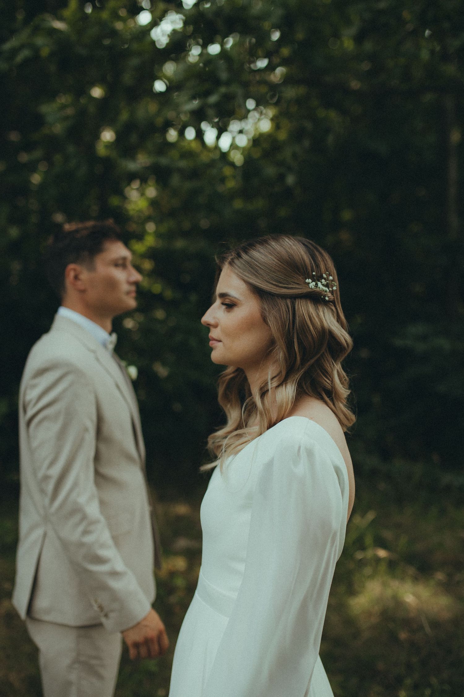A couple in wedding attire poses in a romantic forest setting with soft natural lighting.