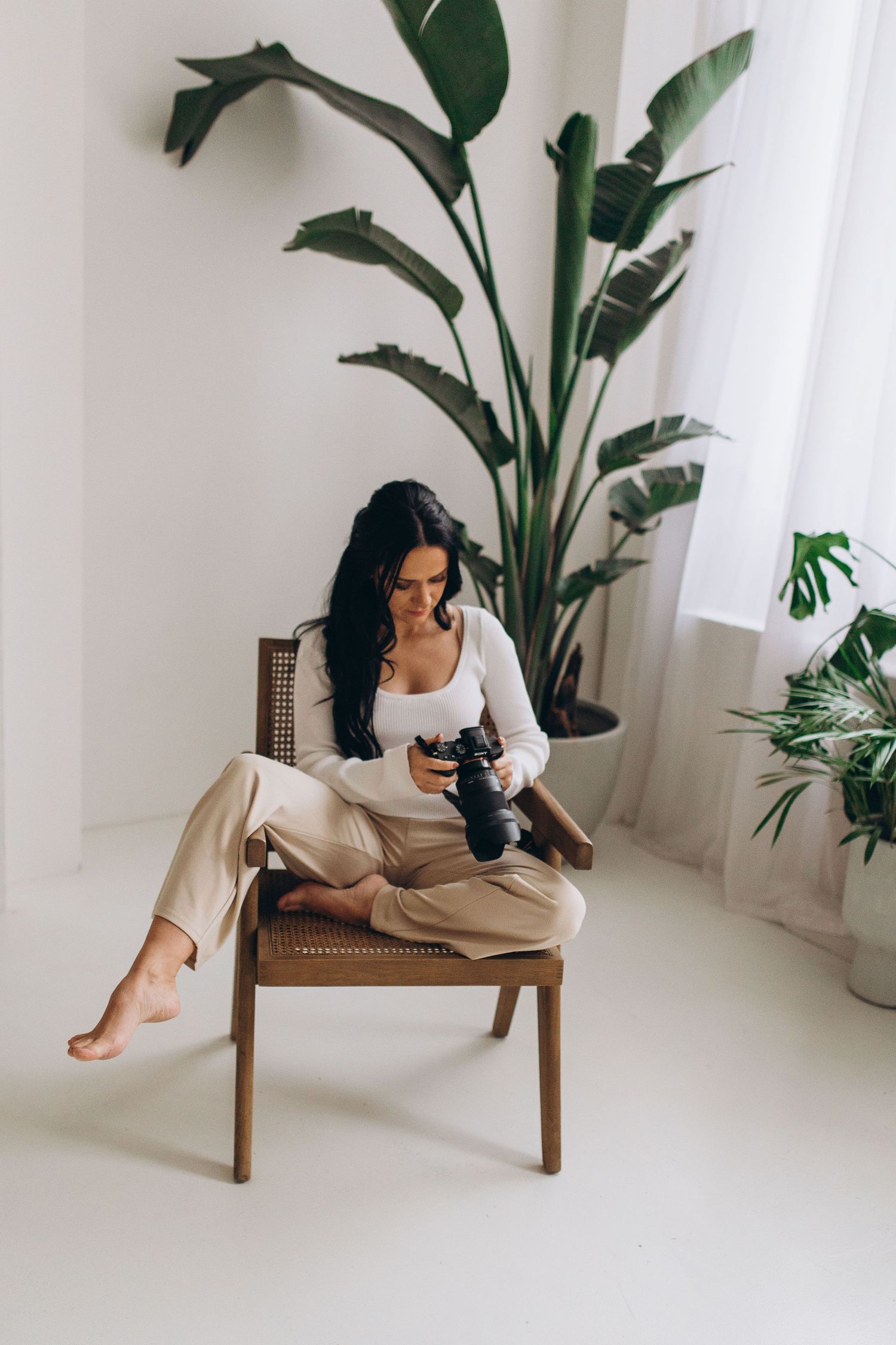 Photographer reviewing camera in modern white room with large tropical plant.