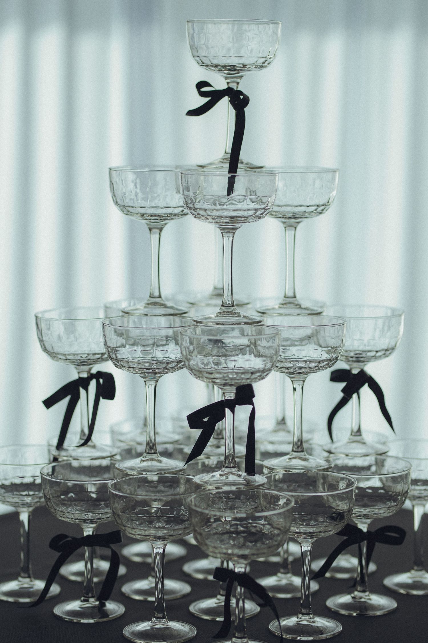 Crystal champagne glasses decorated with black ribbons arranged on a reflective surface.