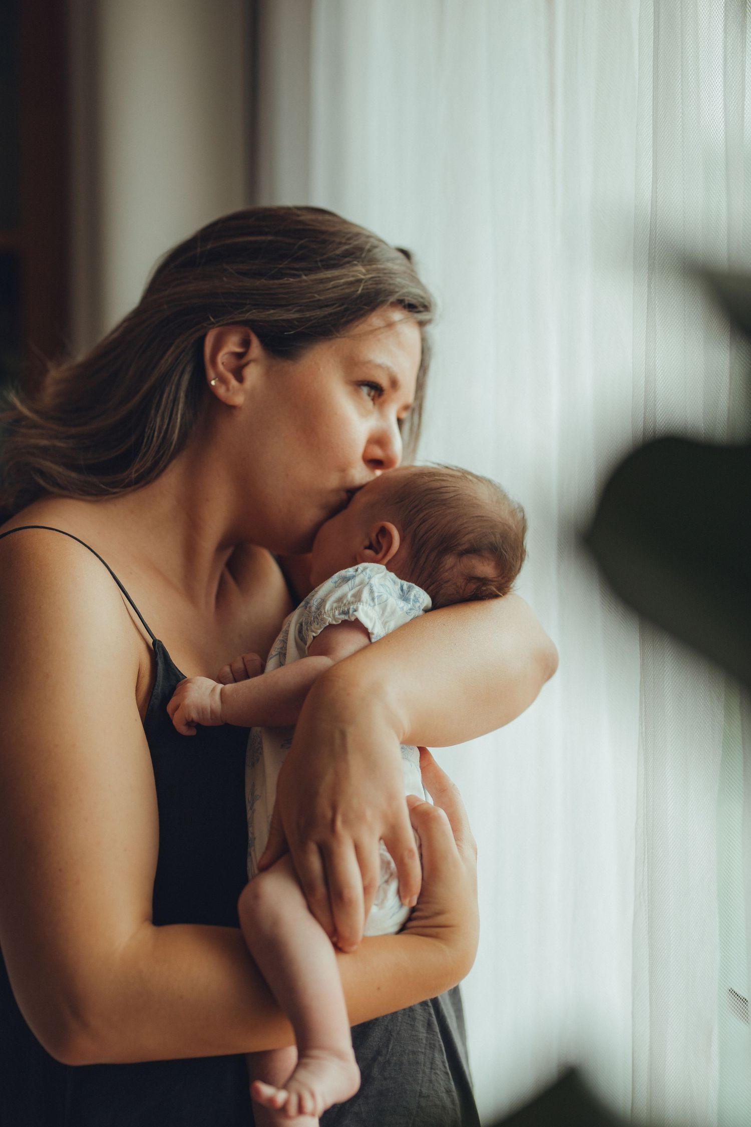 Mother embracing newborn baby against soft window light.