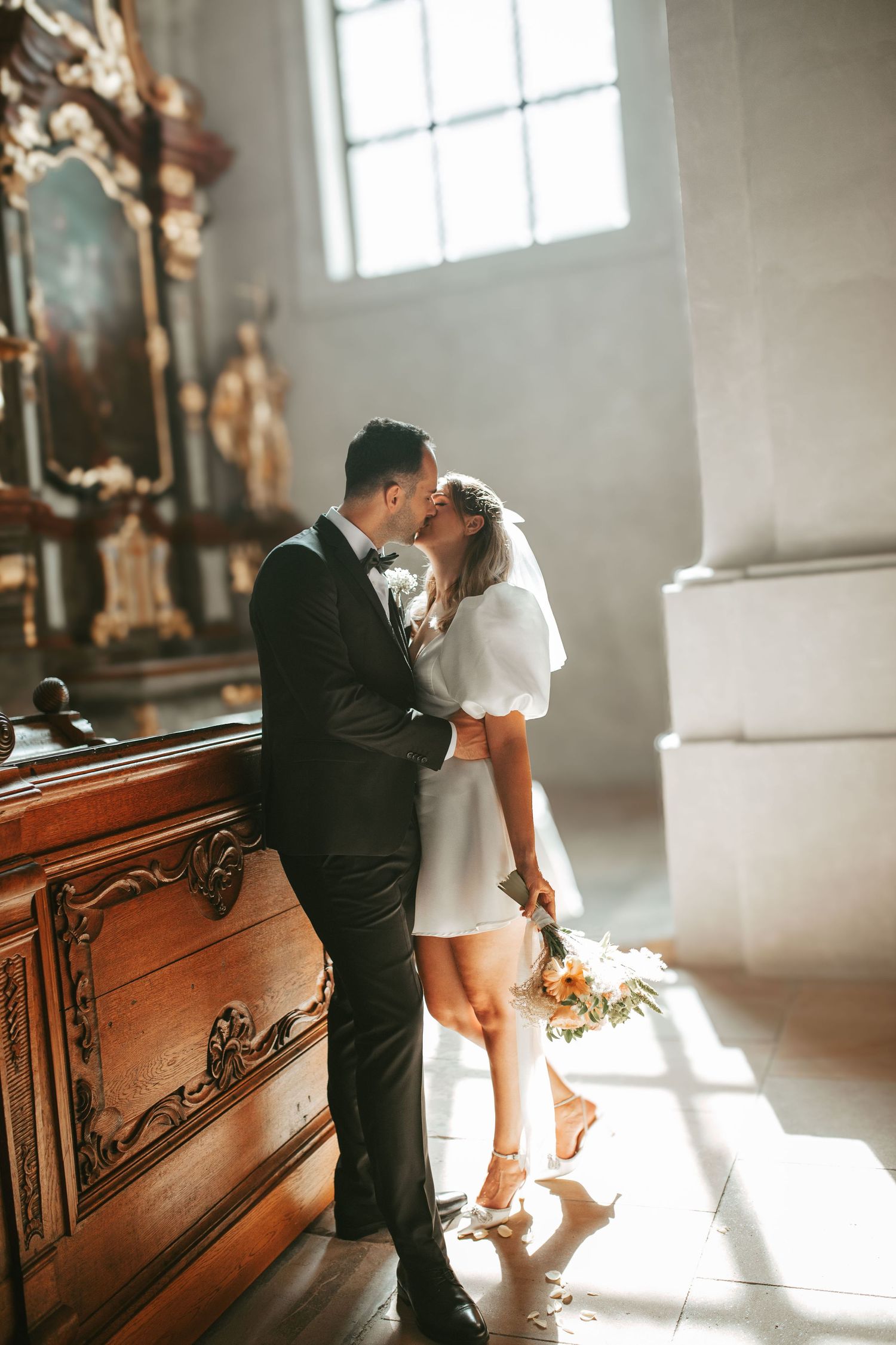 Intimate moment between newlyweds in church with dramatic lighting and wooden details.