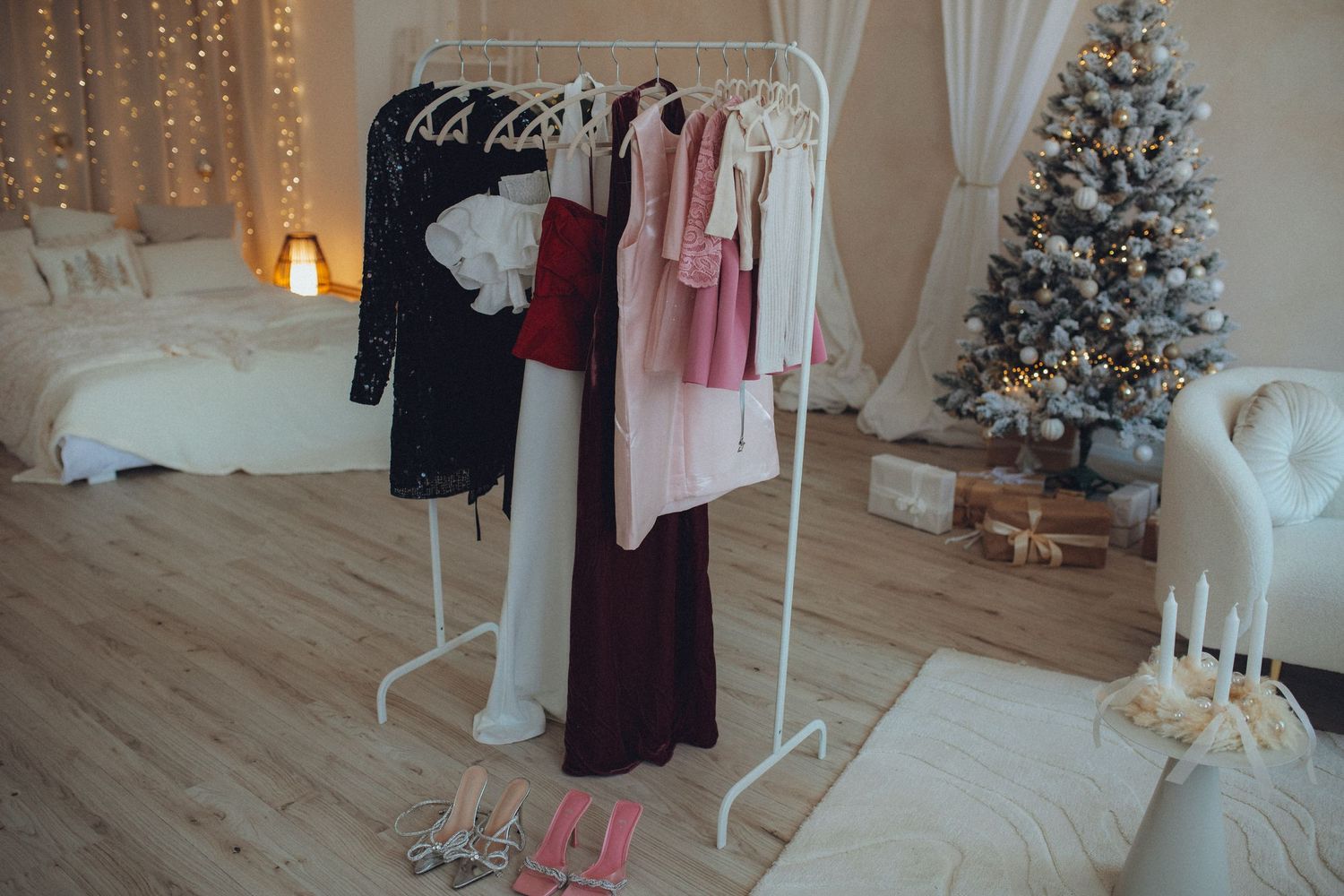 Cozy bedroom corner decorated for Christmas with white clothing rack, lit tree and warm string lights.