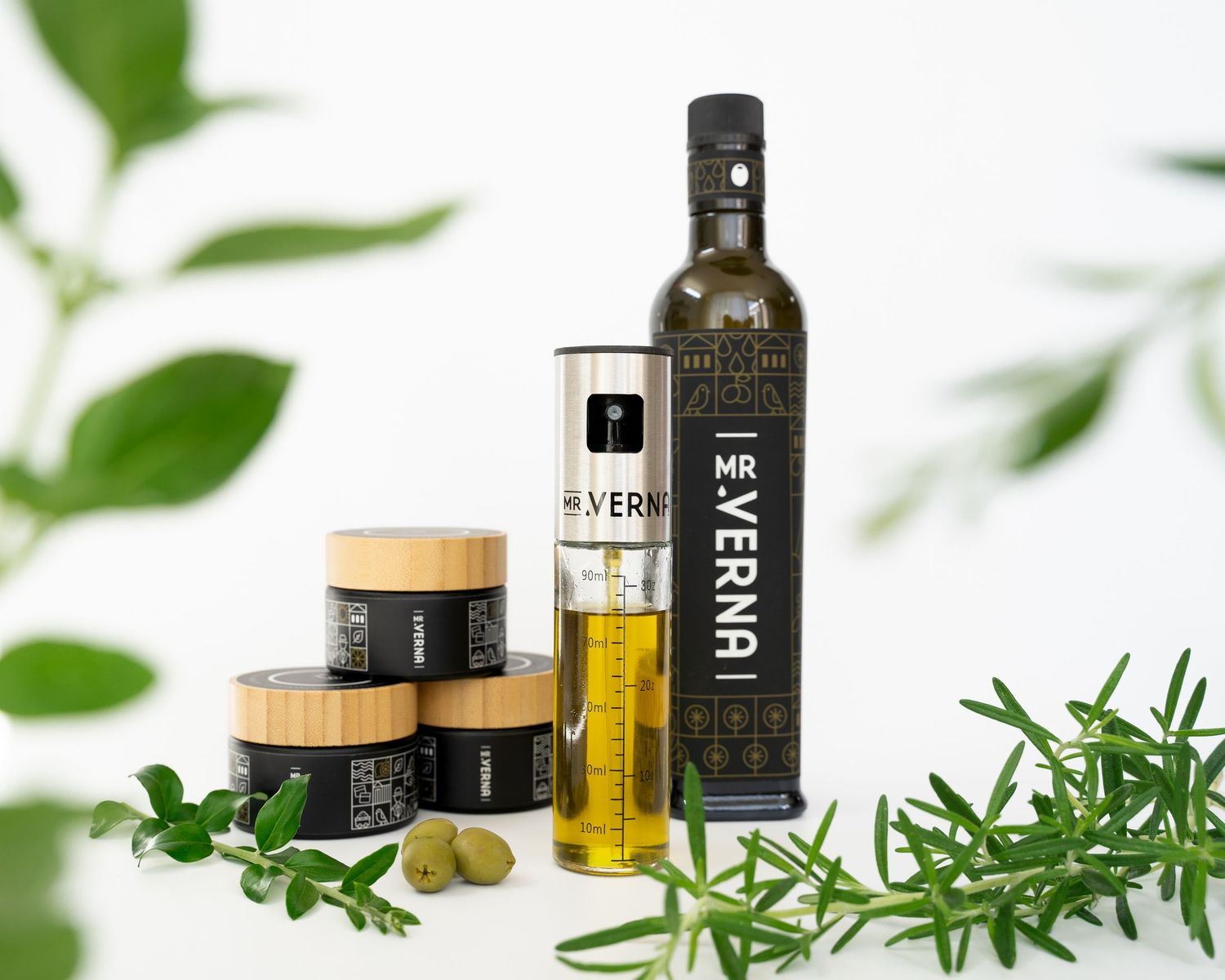 Olive oil bottles, herbs, and green olives arranged on a white surface with natural lighting.