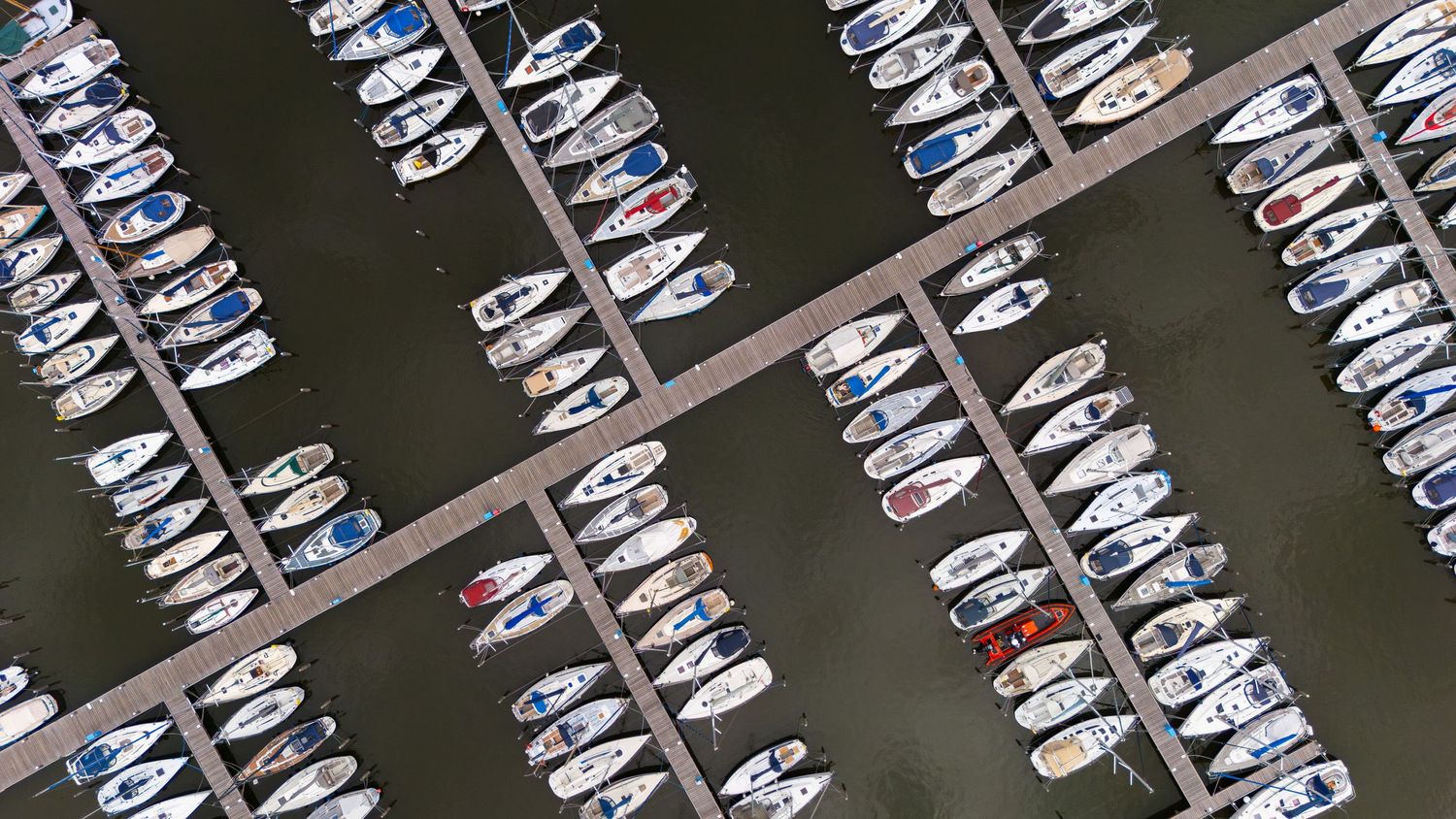 Aerial view of boats and yachts neatly docked in rows at a marina, seen from directly above.