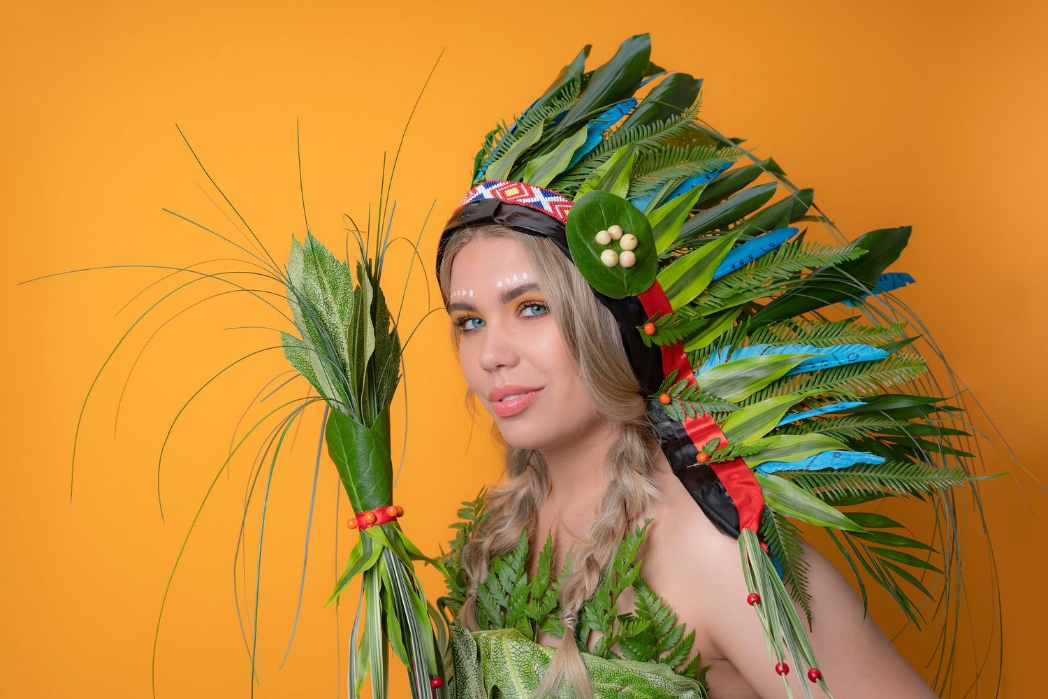 Vibrant tropical photo shoot setup with exotic green feathers against orange background.
