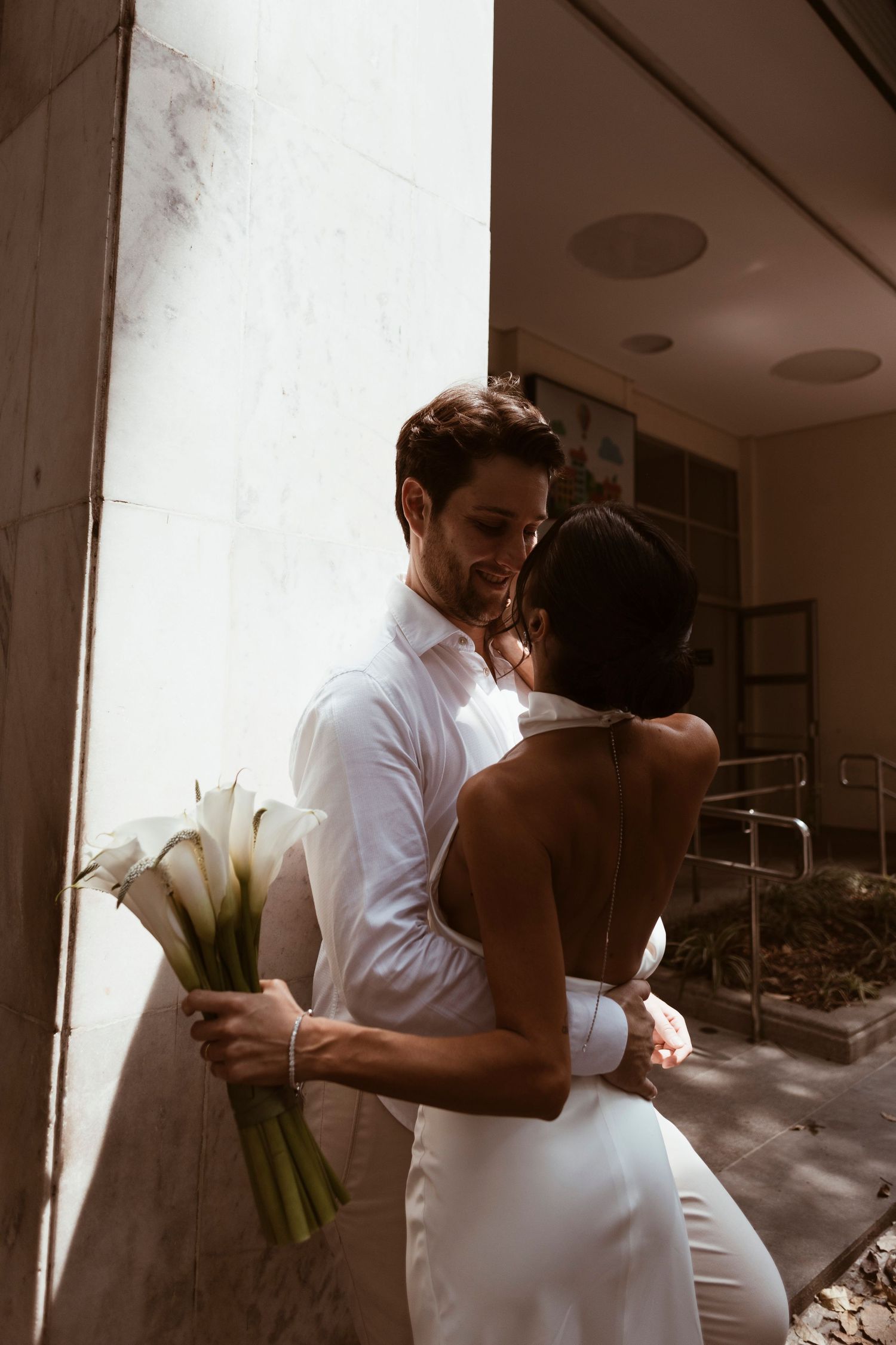 Romantic wedding moment with couple embracing while holding white calla lily bouquet.