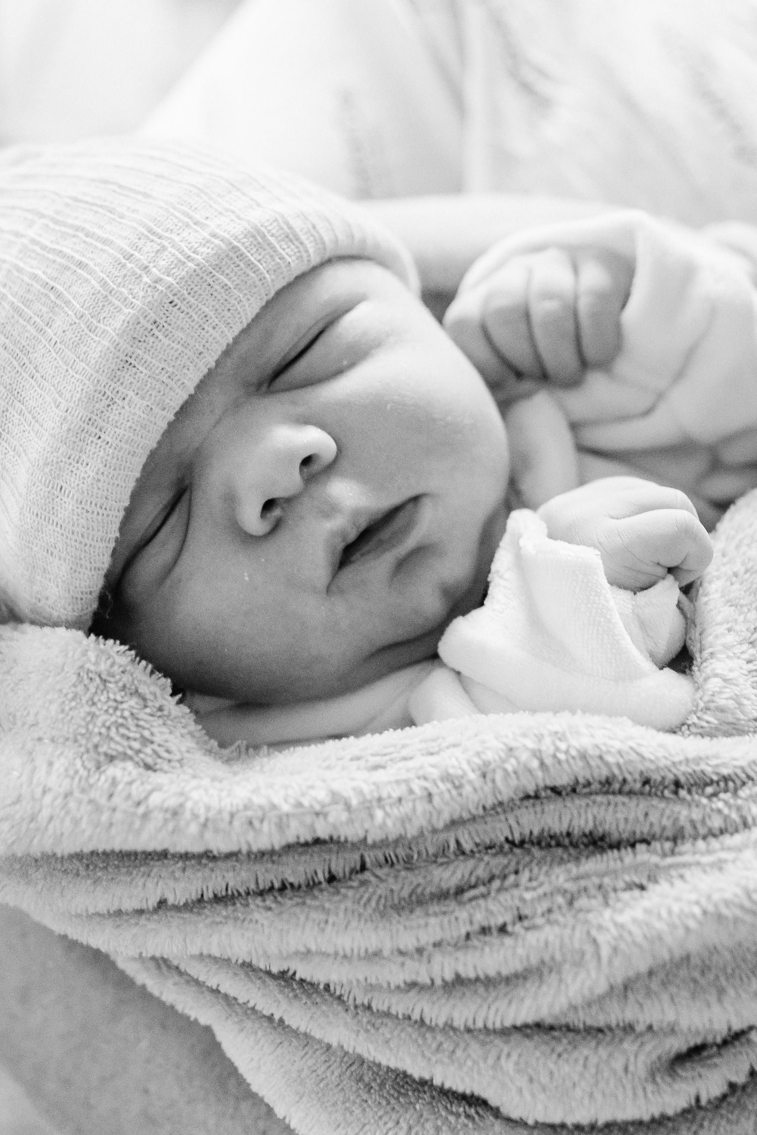 Sleeping newborn wrapped in soft towel wearing white knit cap in black and white.