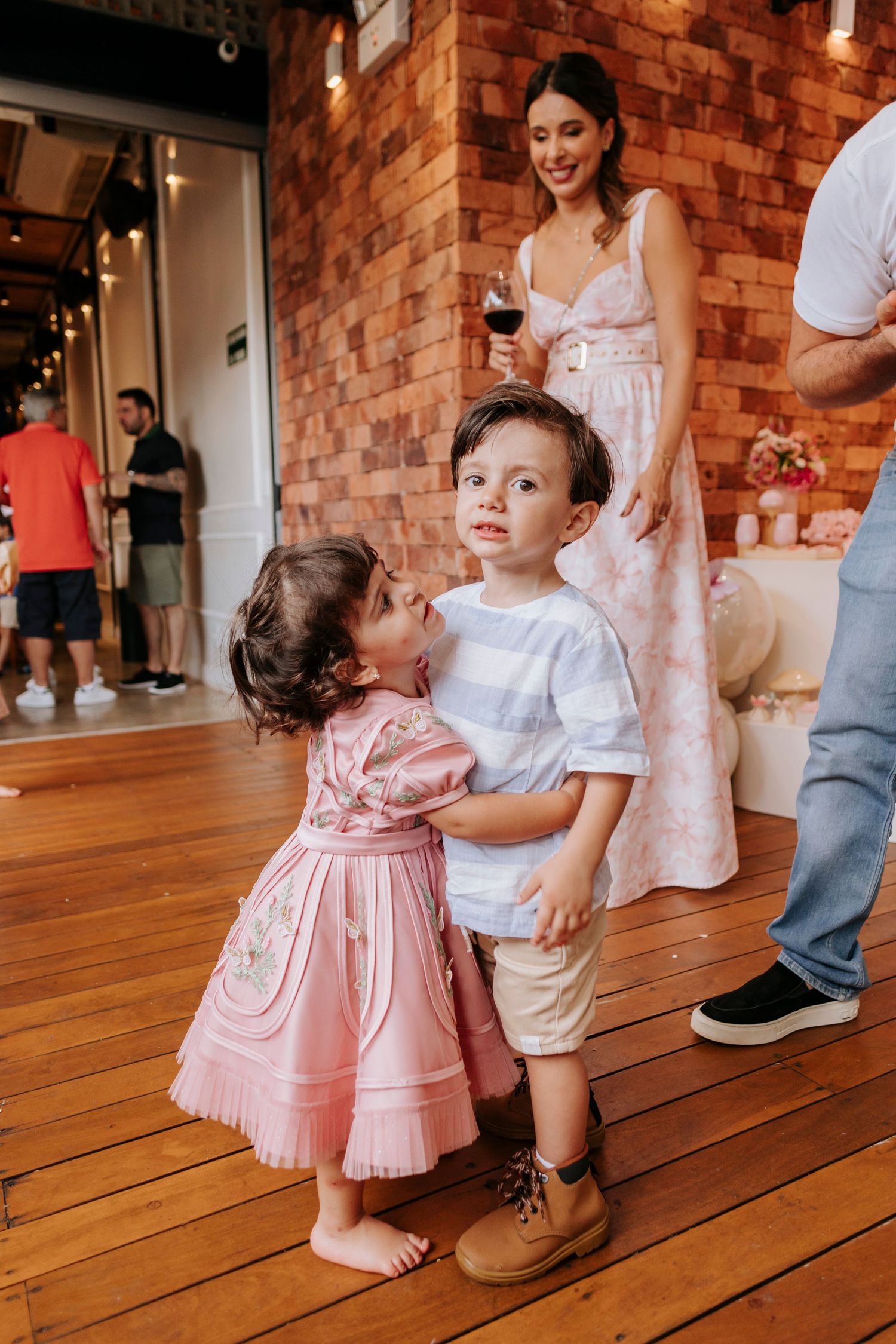 Sweet candid moment at party with exposed brick wall and wooden floors.
