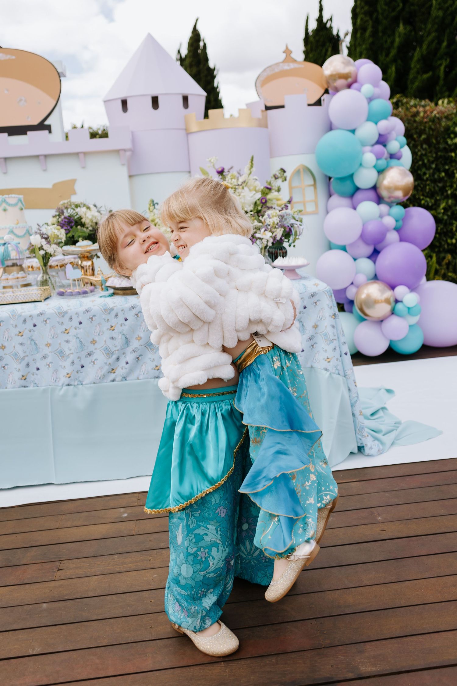 A whimsical party scene with balloon arches and a castle backdrop on a wooden deck.