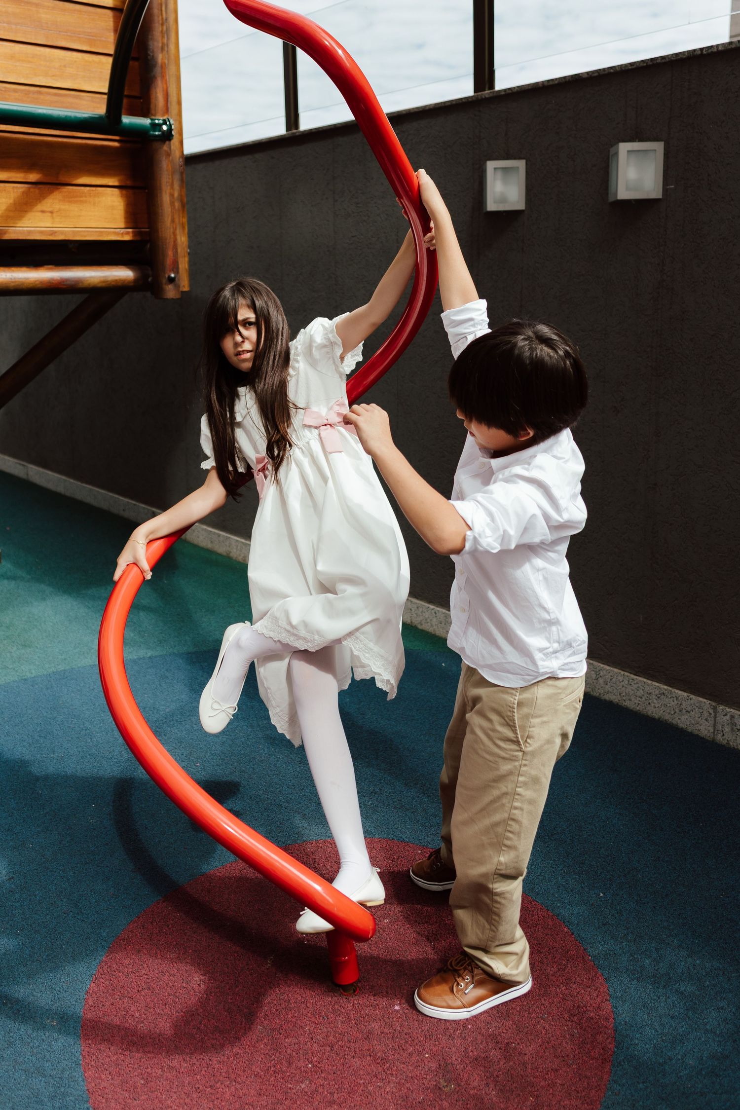 Children play with a large red foam noodle in a classroom setting with dark walls.