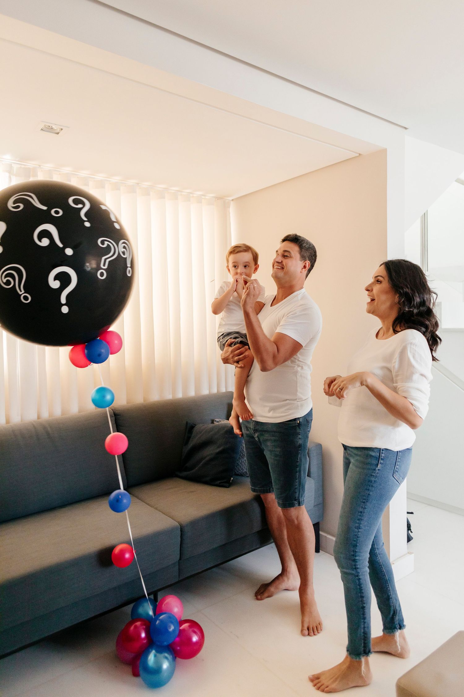 A gender reveal party scene with black question mark balloons and blue and pink decorations in a modern living room.