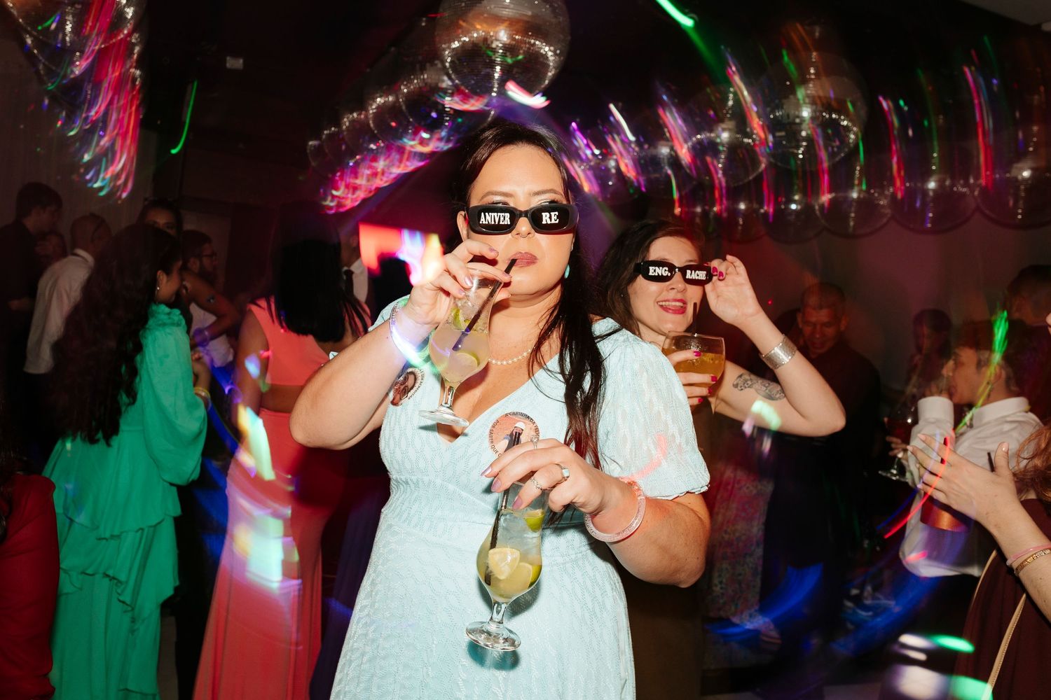 Party scene with colorful lights and dancing people in a nightclub atmosphere enjoying drinks and festivities.