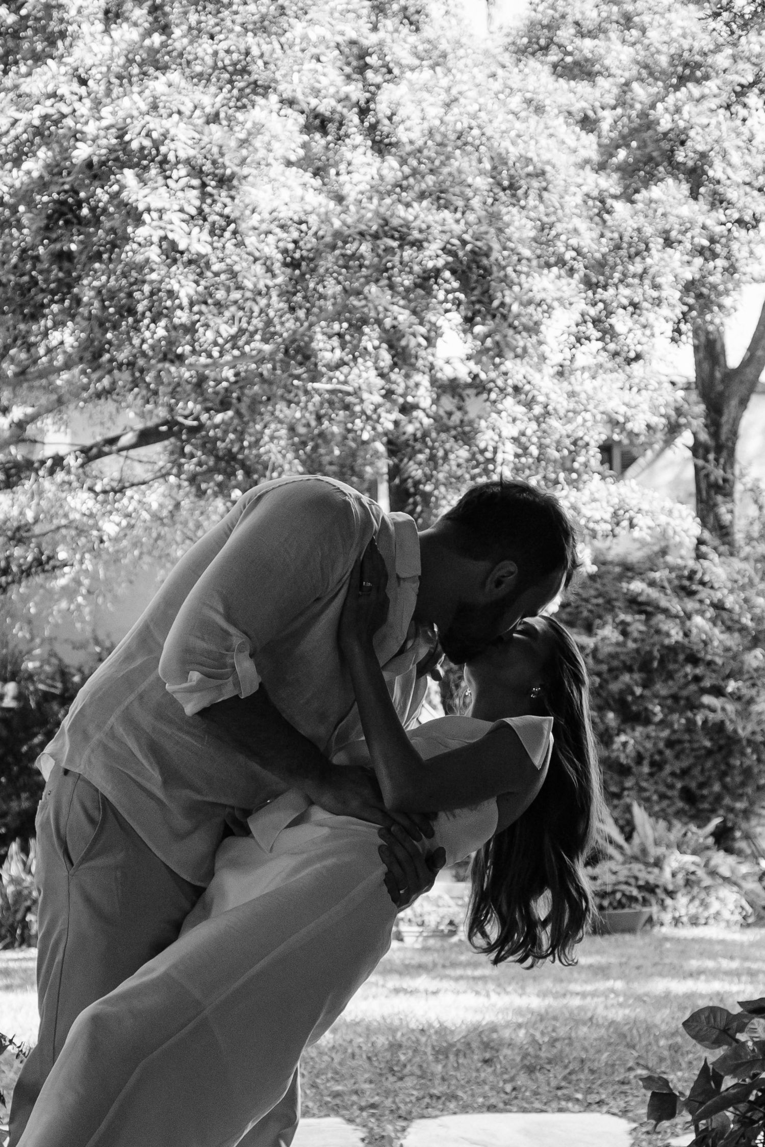 A romantic black and white photo of a couple sharing an intimate dip pose outdoors.