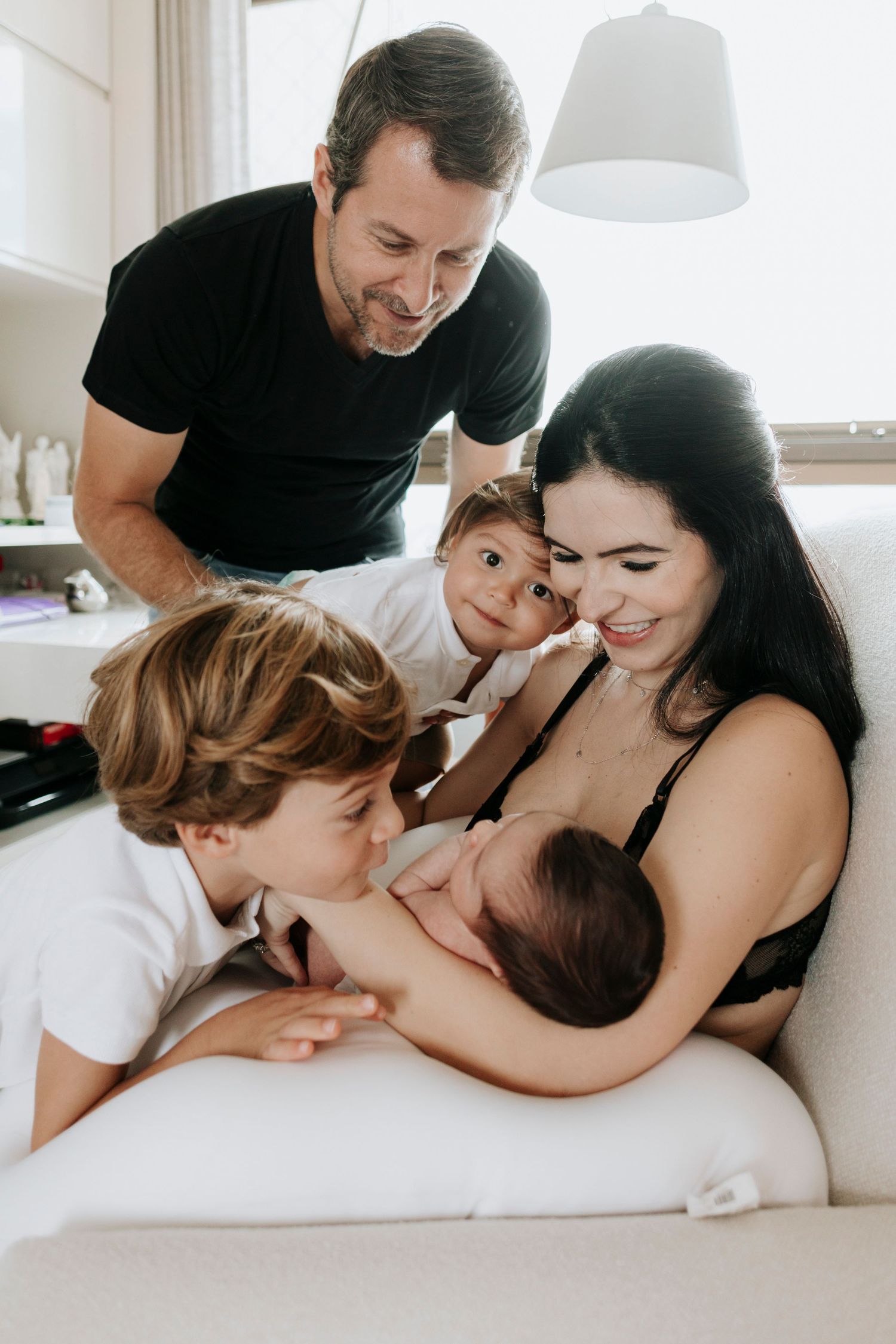 Family shares intimate moment gathered around newborn baby during feeding time on white couch.