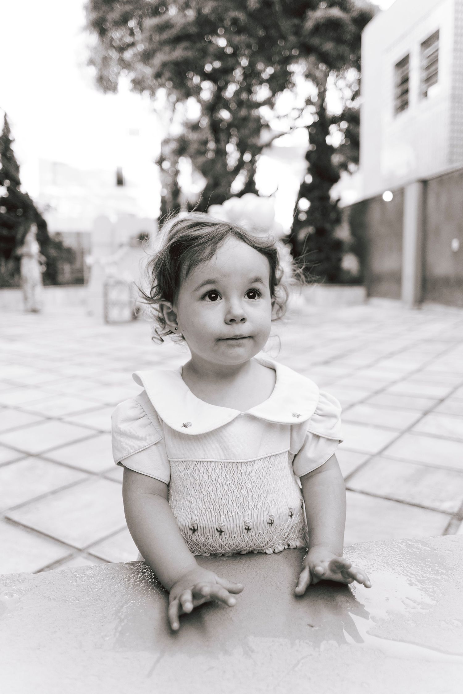 A candid black and white portrait of a child in a smocked dress.