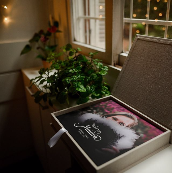 Elegant photo book in a luxury gift box near a window with festive lights and green plants.