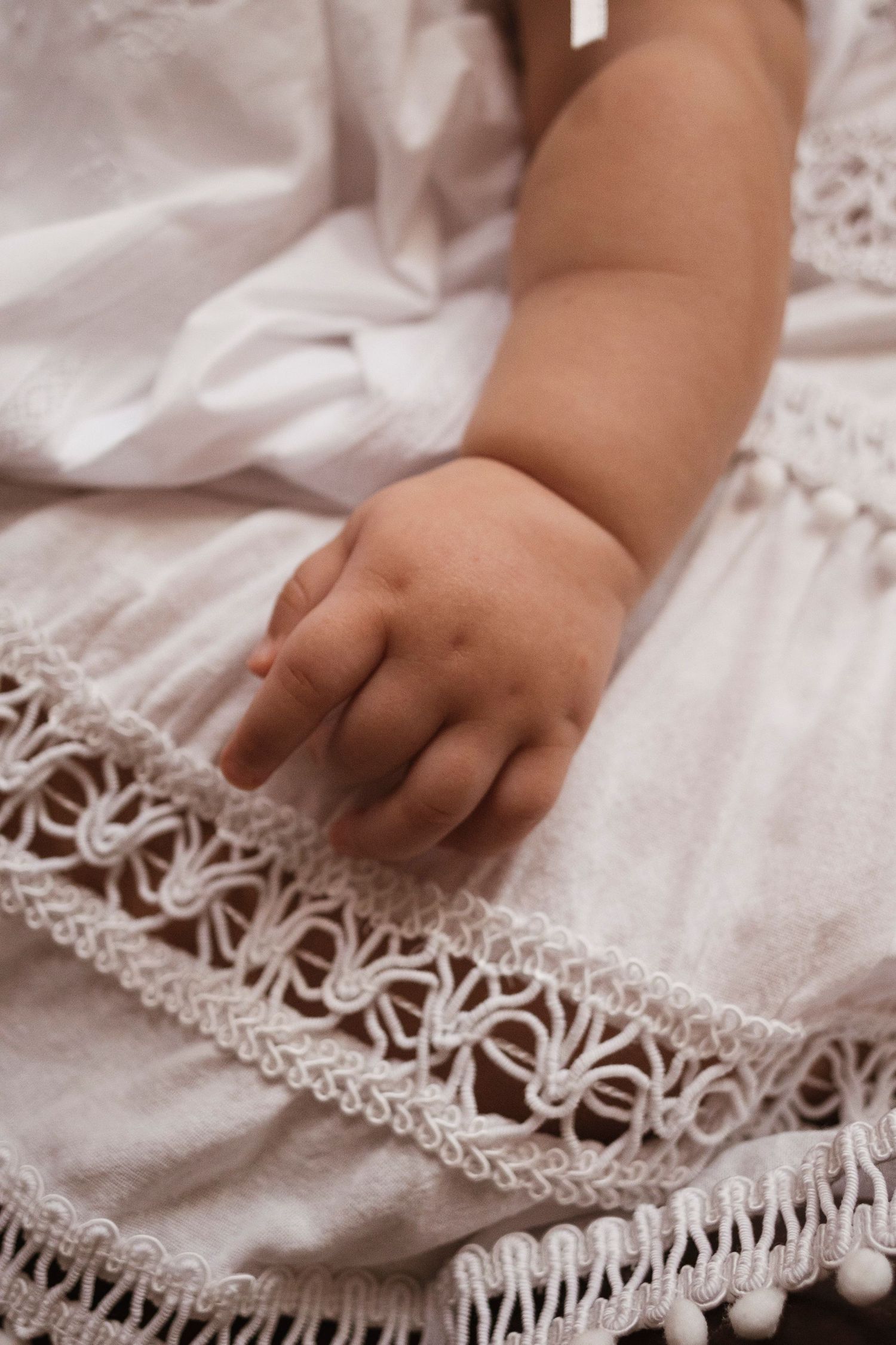 Close-up of baby's hand resting on white lace christening gown.
