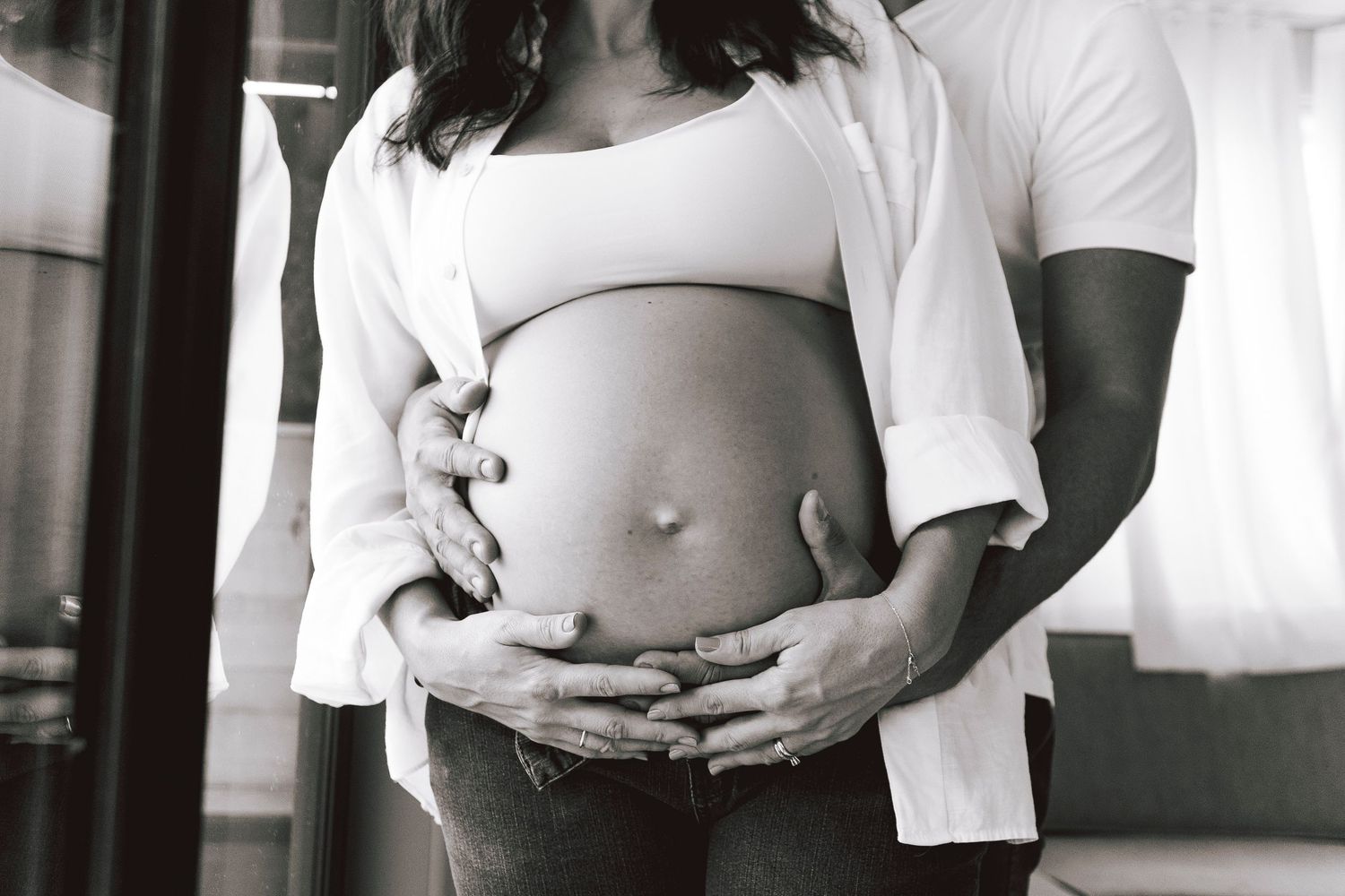 Intimate black and white maternity photo showing hands cradling pregnant belly.