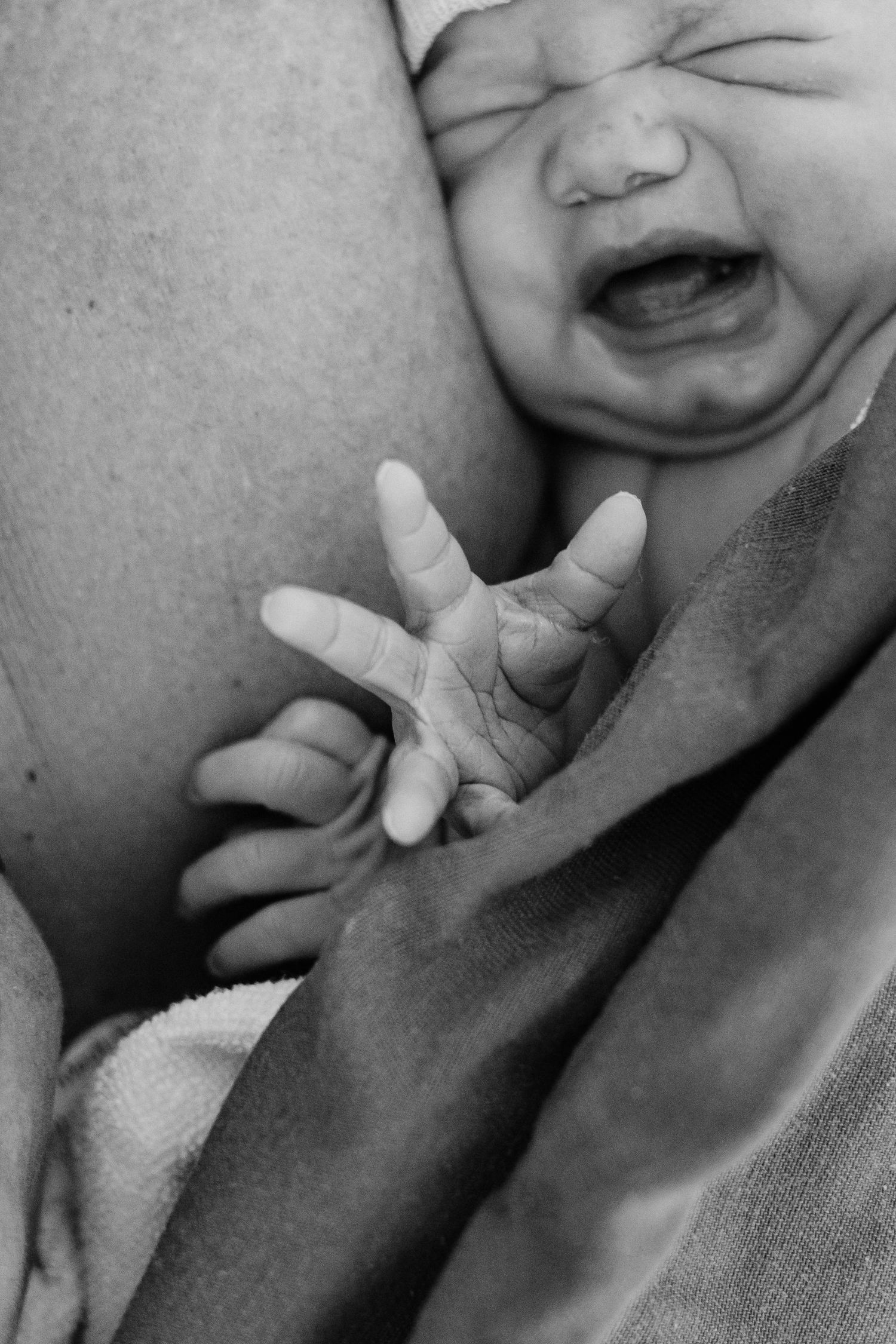 Close up black and white photo of a newborn's hand and face showing strong emotion.