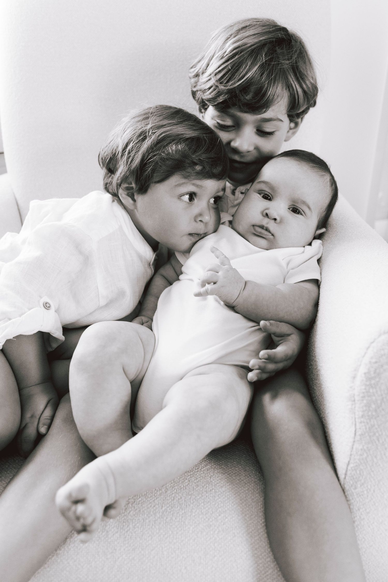 Three young siblings share an intimate moment on a white background.