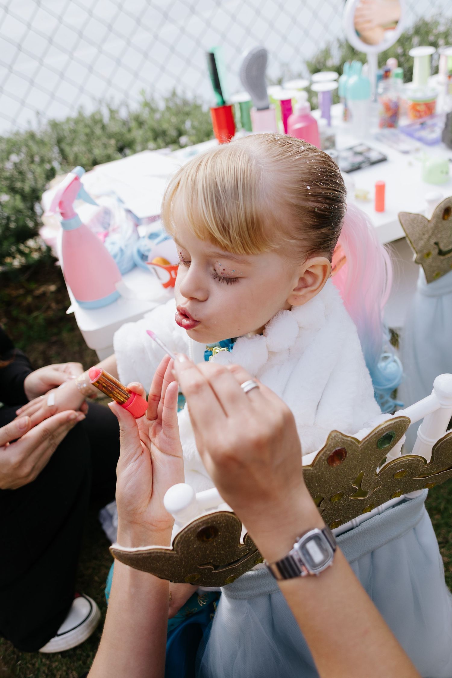 A festive party setting with someone getting their face painted while wearing a white top.