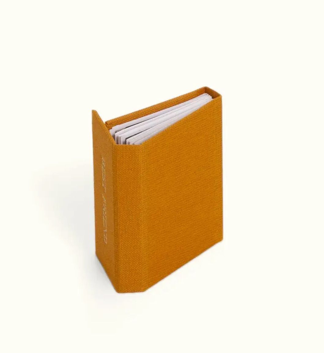 Small mustard yellow hardcover mini notebook with white pages, standing upright on a white background.