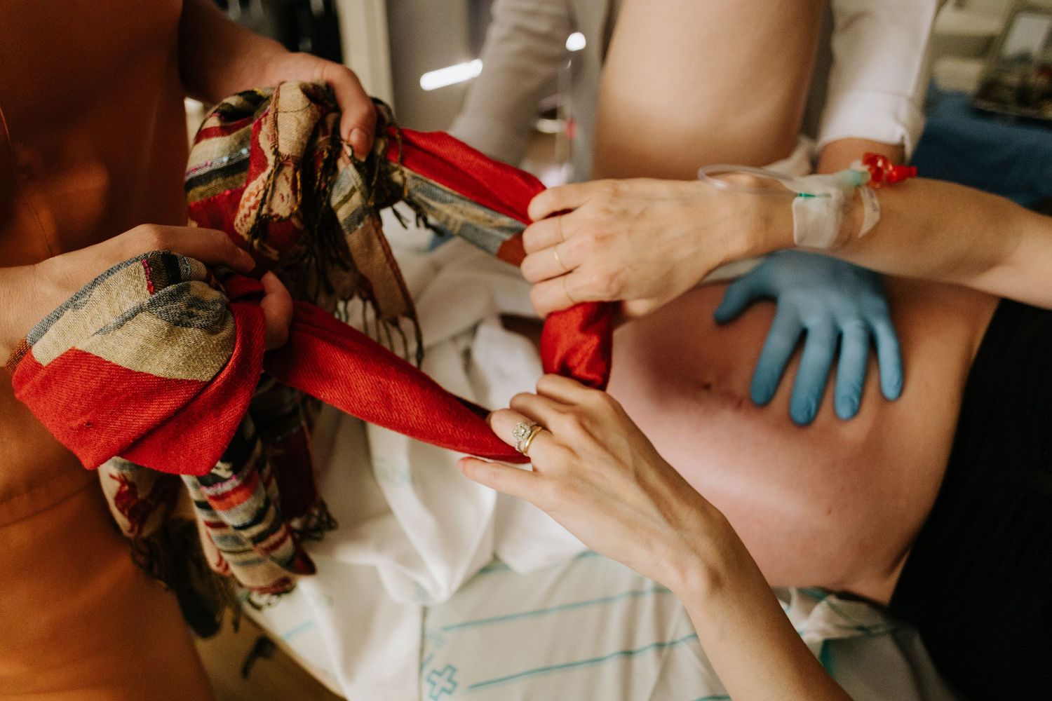 Medical staff assist a pregnant woman during labor, with blue gloves and a colorful cloth visible in a clinical setting.