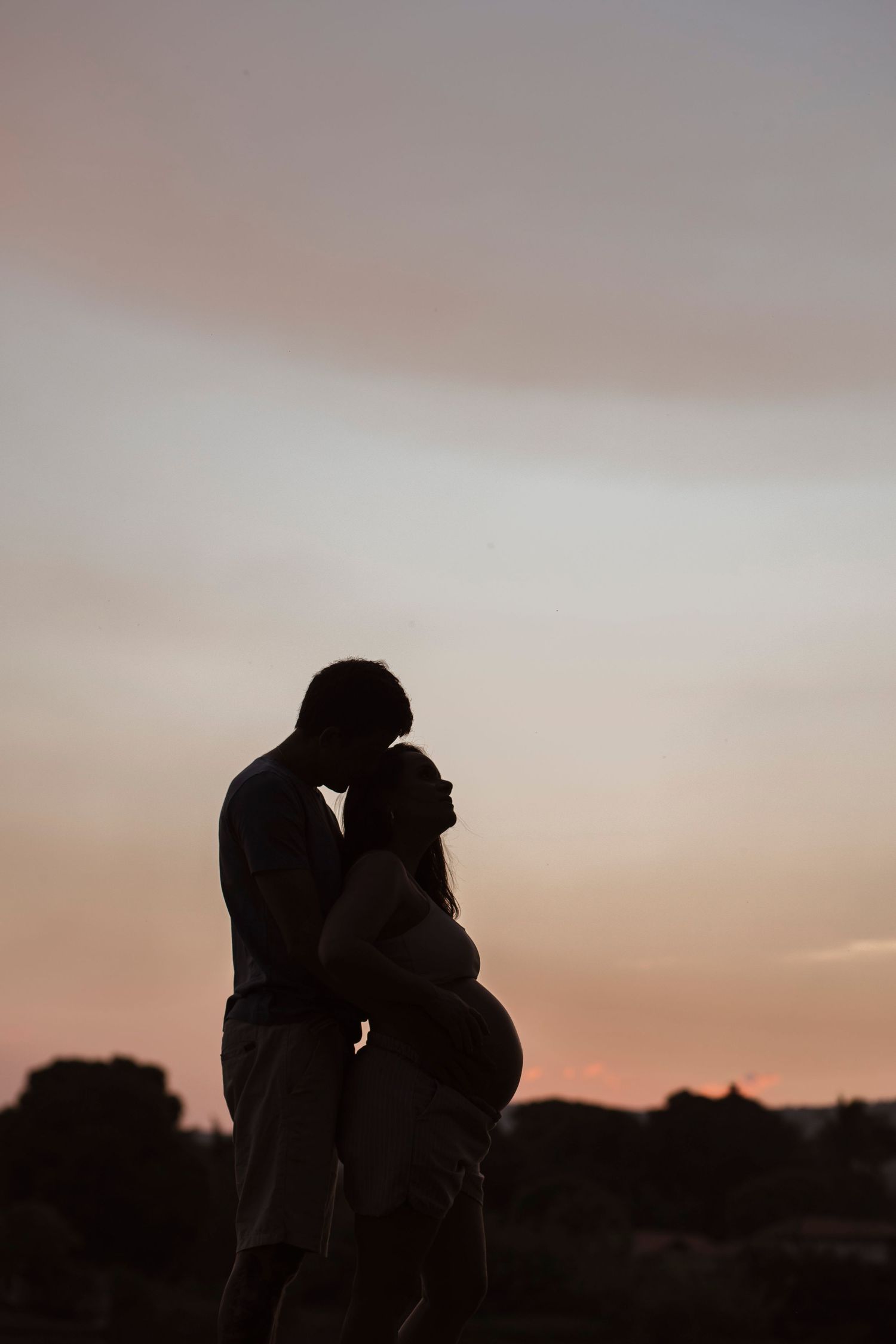 Silhouetted couple embracing during sunset maternity photoshoot.