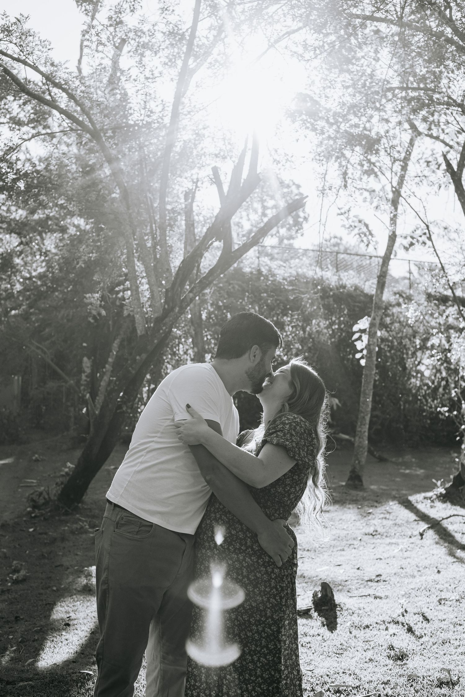Couple embracing during sunset maternity photoshoot among trees.