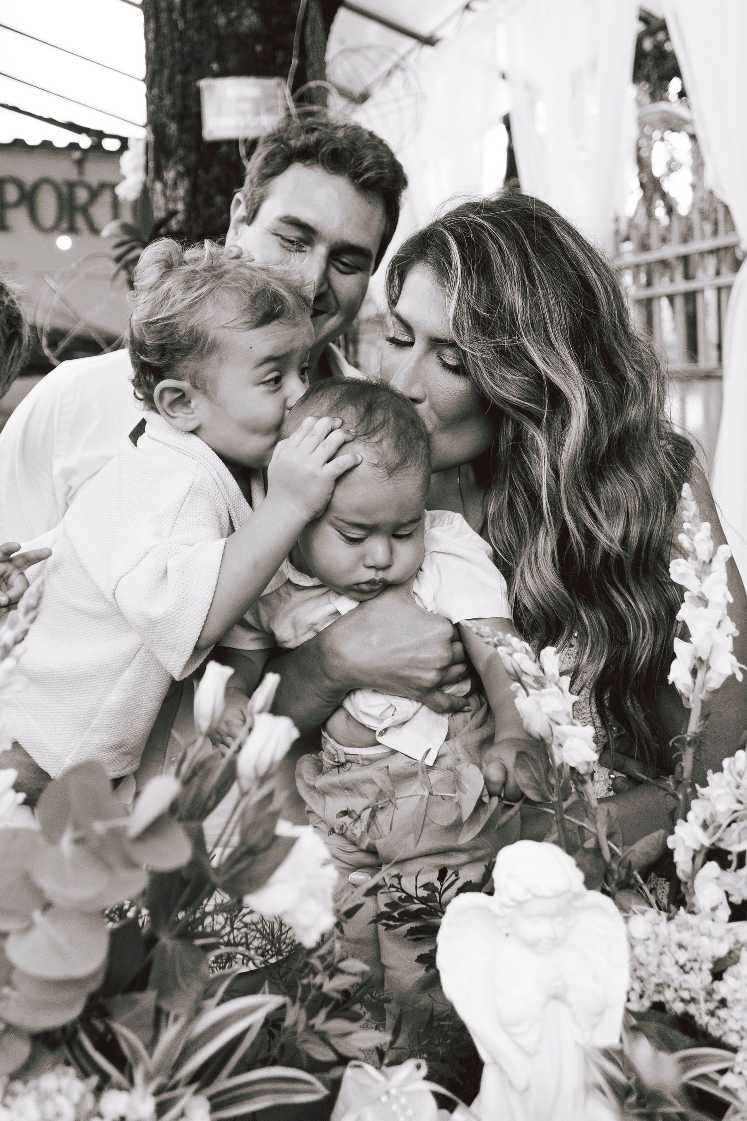 Black and white family portrait showing tender moment with children among flowers outdoors.