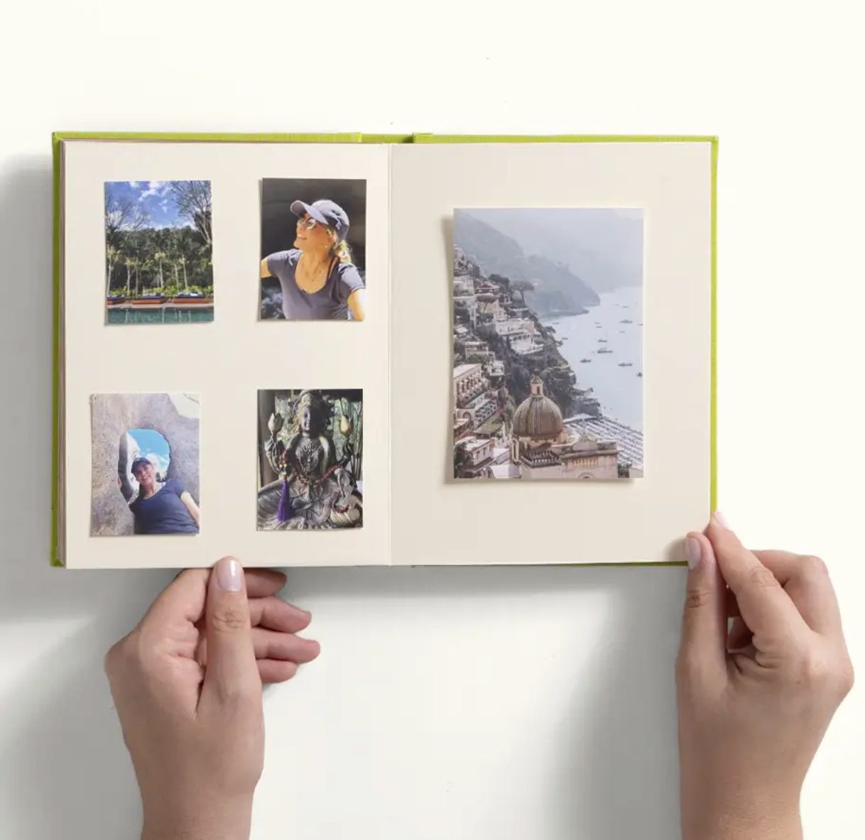 Hands holding an open photo album with travel pictures arranged on cream pages, featuring a green hardcover book.
