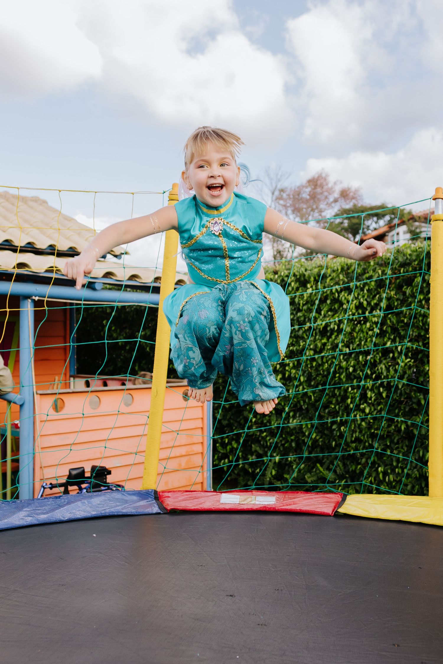 A joyful moment captured mid-jump on a colorful trampoline in a backyard setting.
