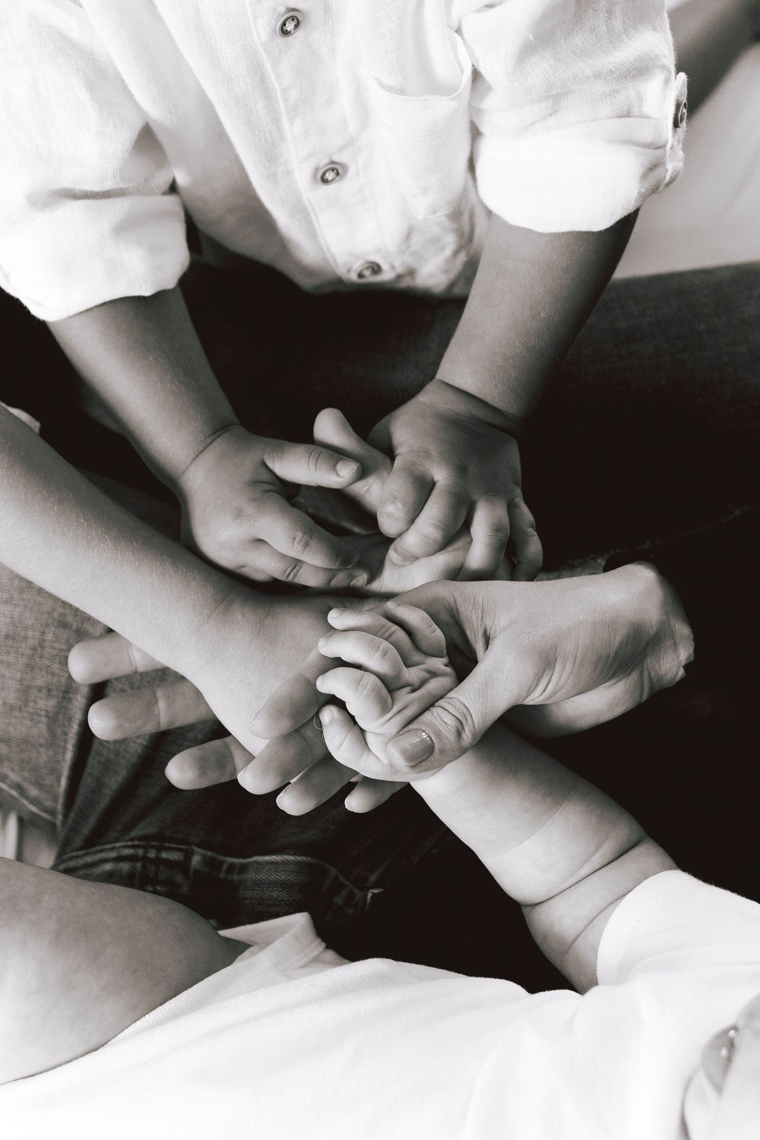 Black and white close-up of multiple hands overlapping in an intimate family portrait.