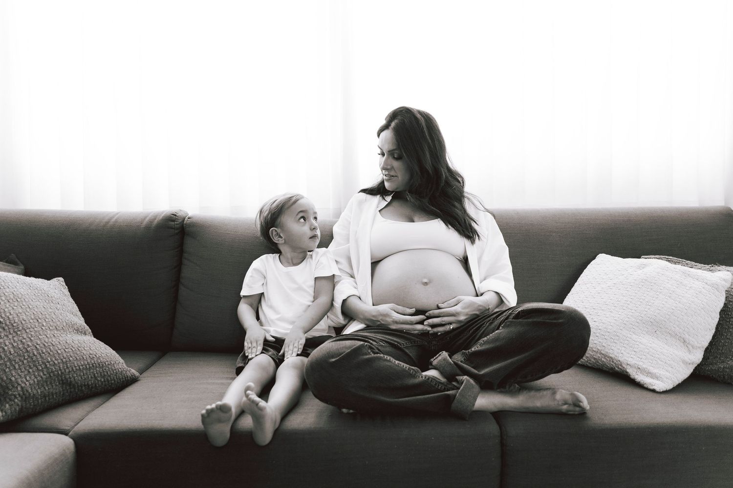 Candid black and white photo of pregnant mother and child sharing moment on couch.