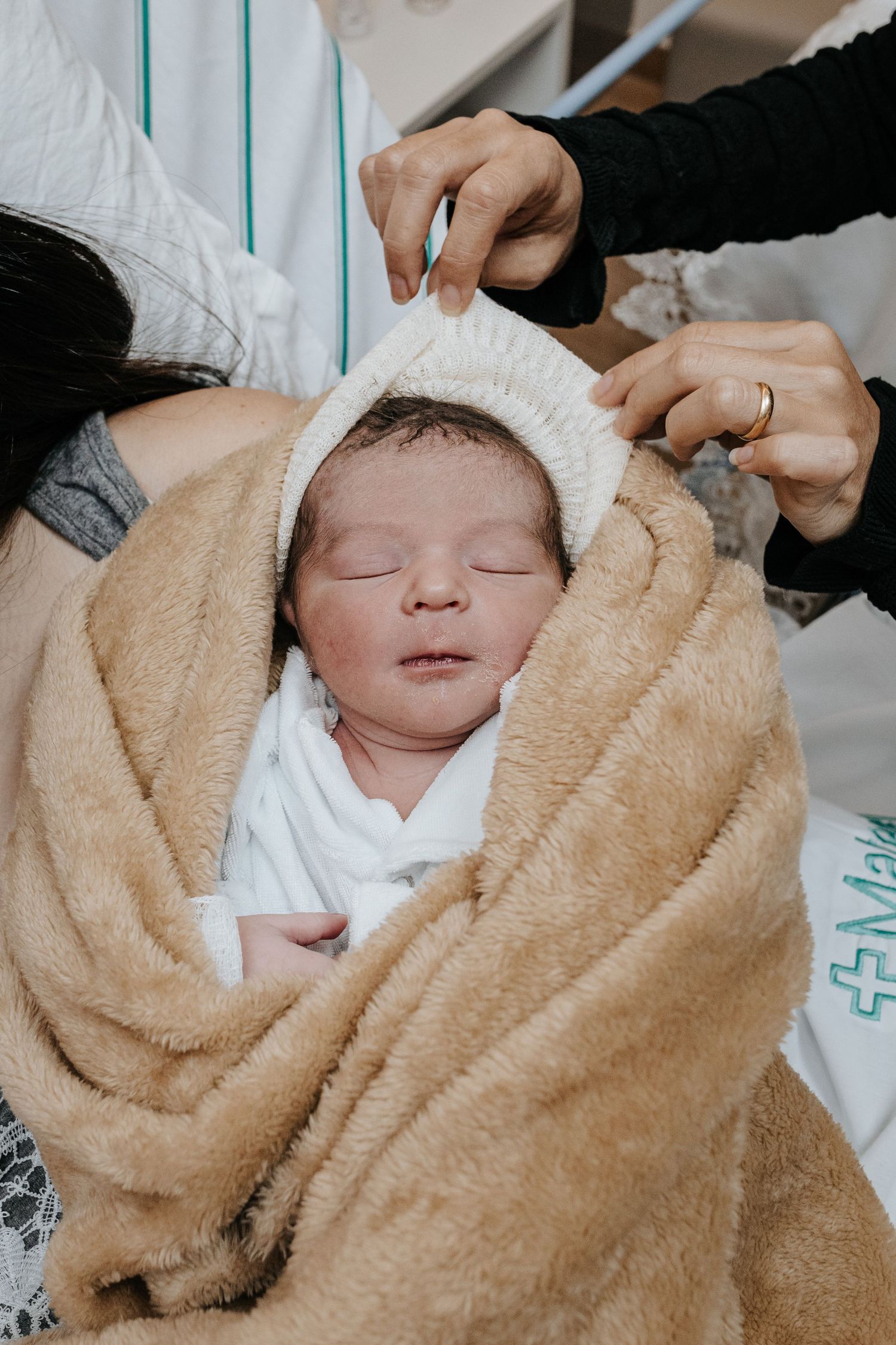 Newborn baby wrapped in soft beige blanket while being examined in hospital.