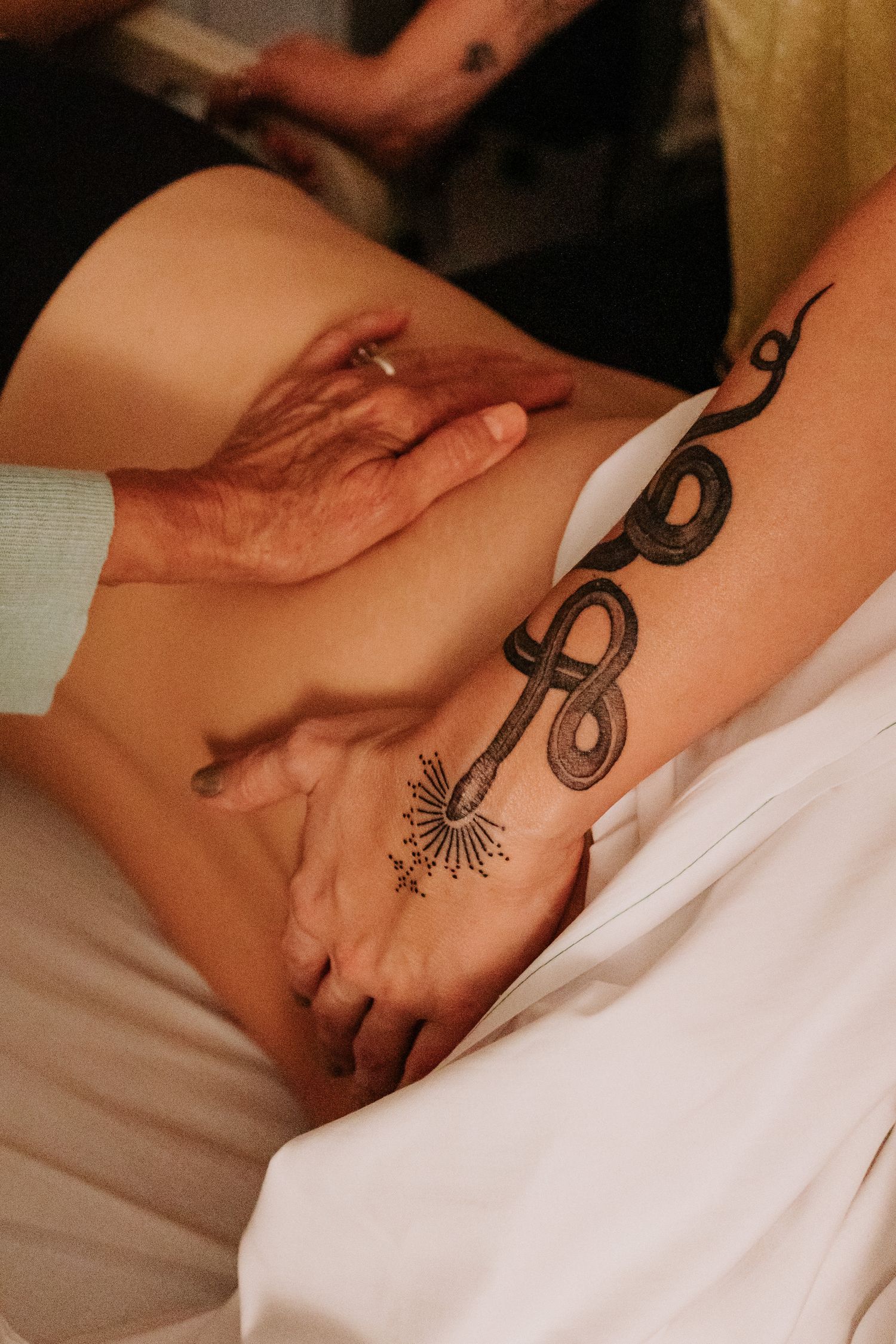 Hands rest on a leg with an ornate decorative tattoo design visible.