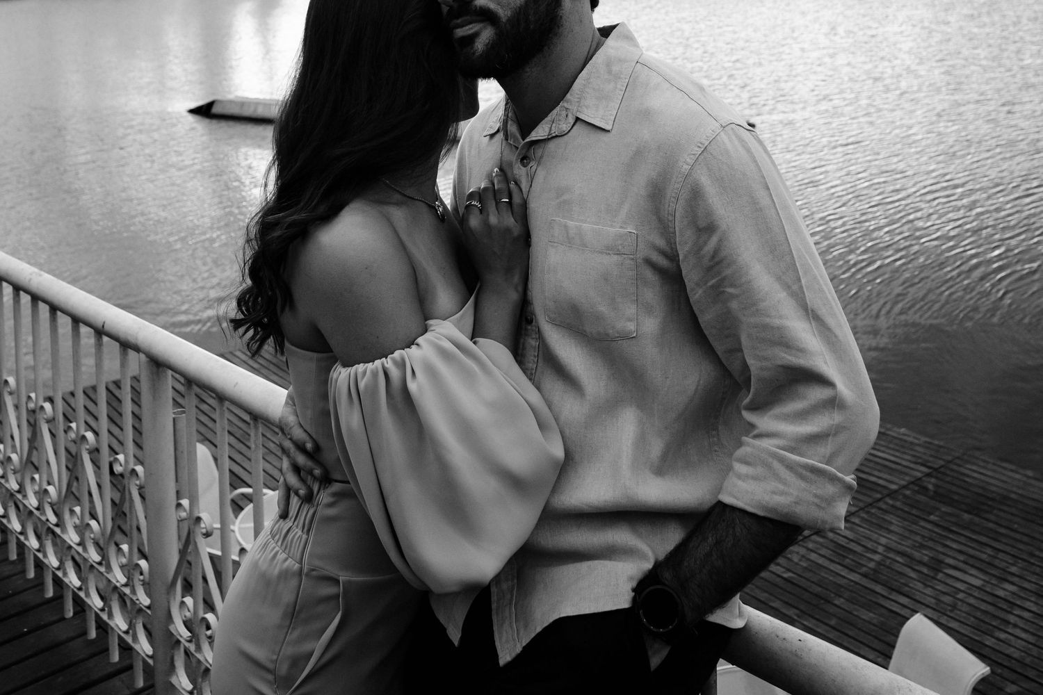 Black and white photo of couple in intimate embrace on waterfront balcony.