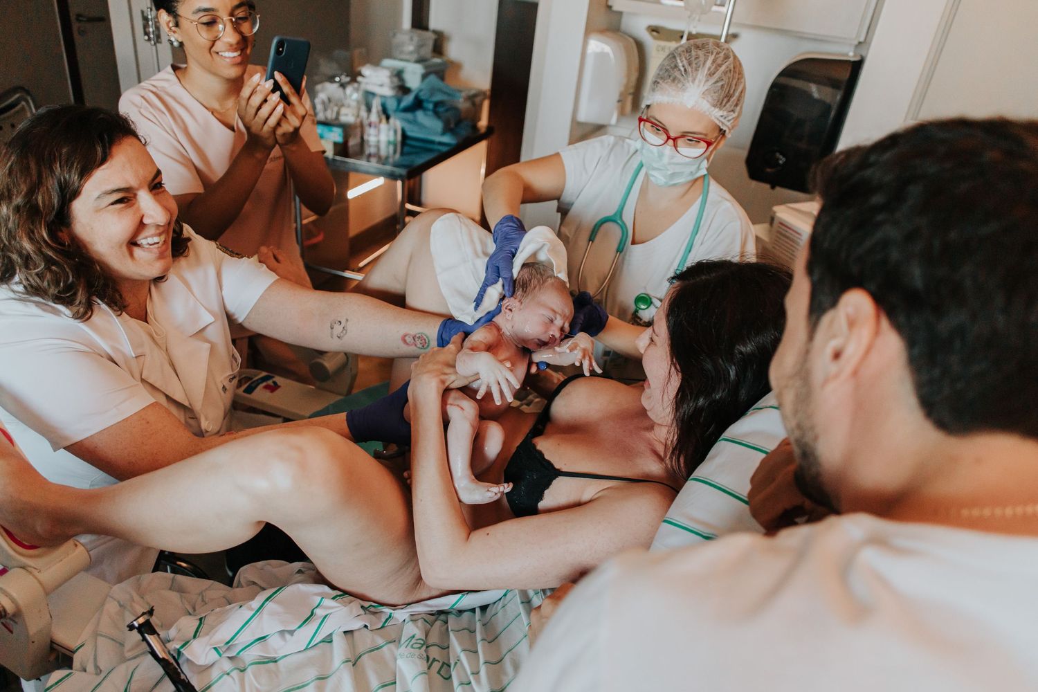 Medical staff gather around a hospital bed during a delivery while wearing protective equipment.