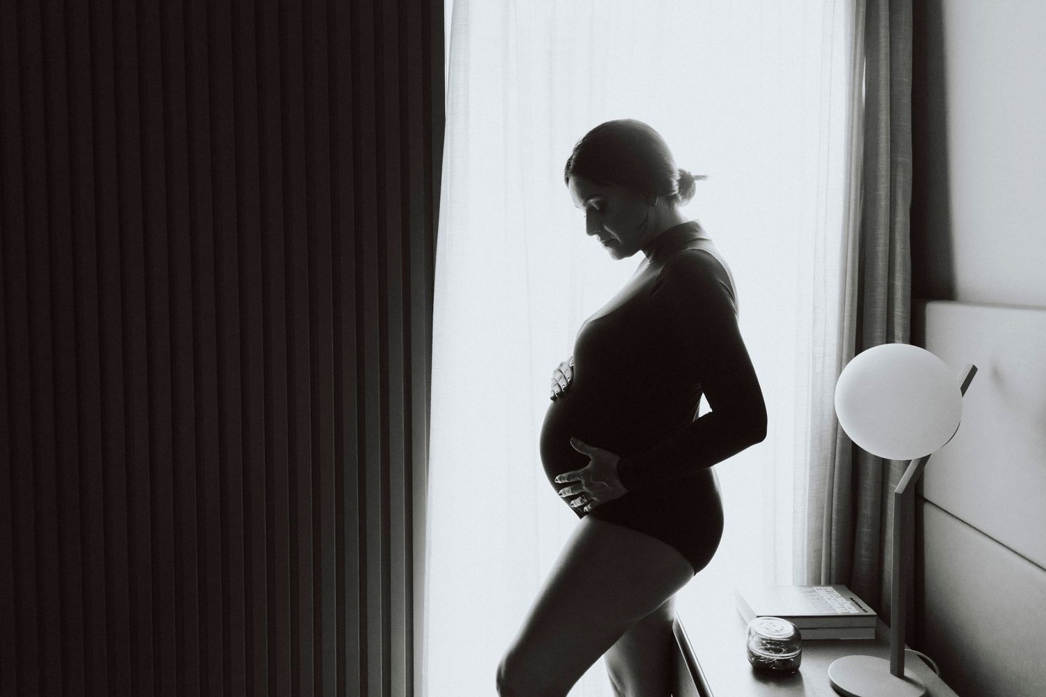 Silhouette of pregnant woman in profile against window light creating dramatic maternity portrait.
