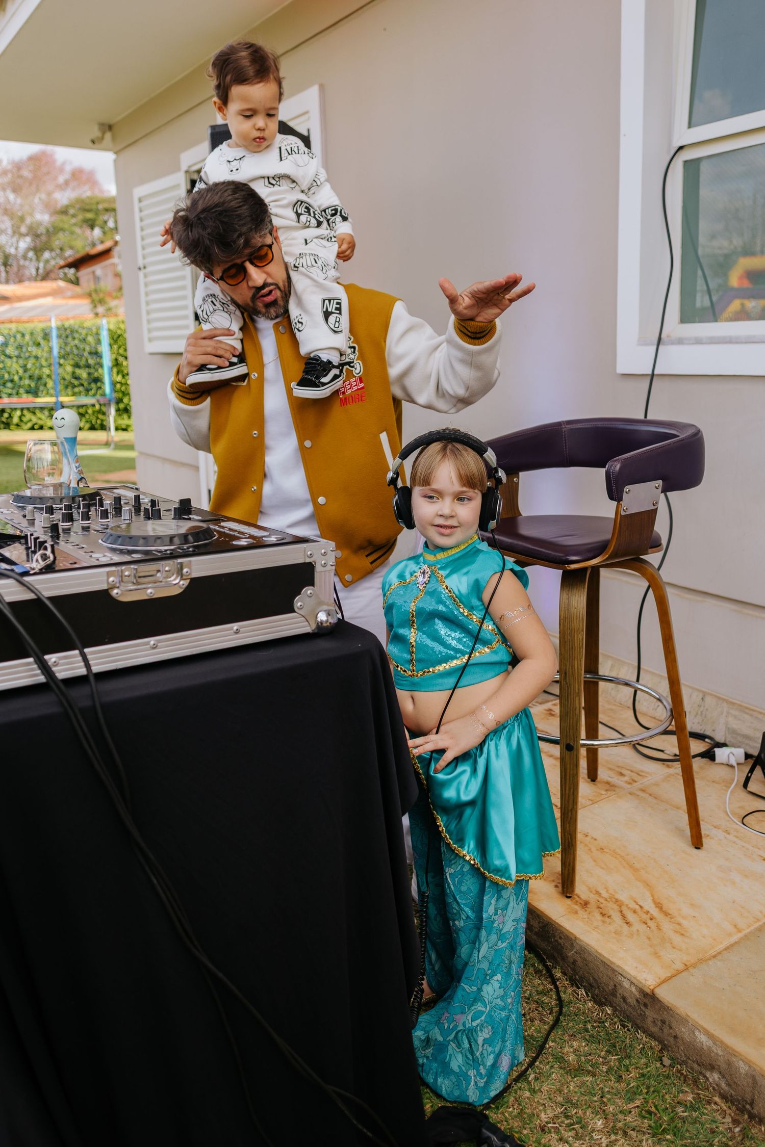 A child in a turquoise dress dances and twirls while playing near a black table during an outdoor gathering.