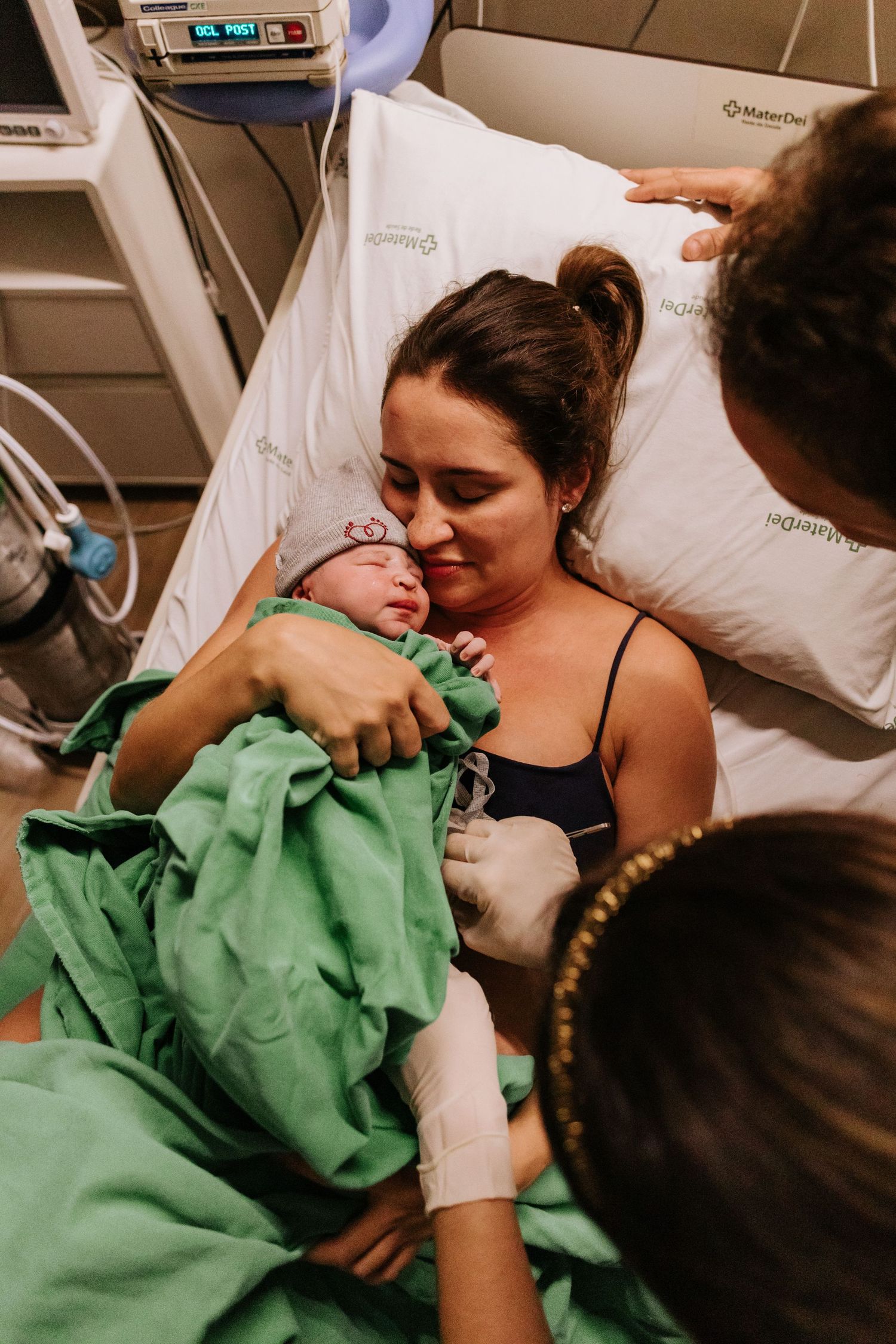 A touching moment between parent and newborn in a hospital bed surrounded by medical equipment.
