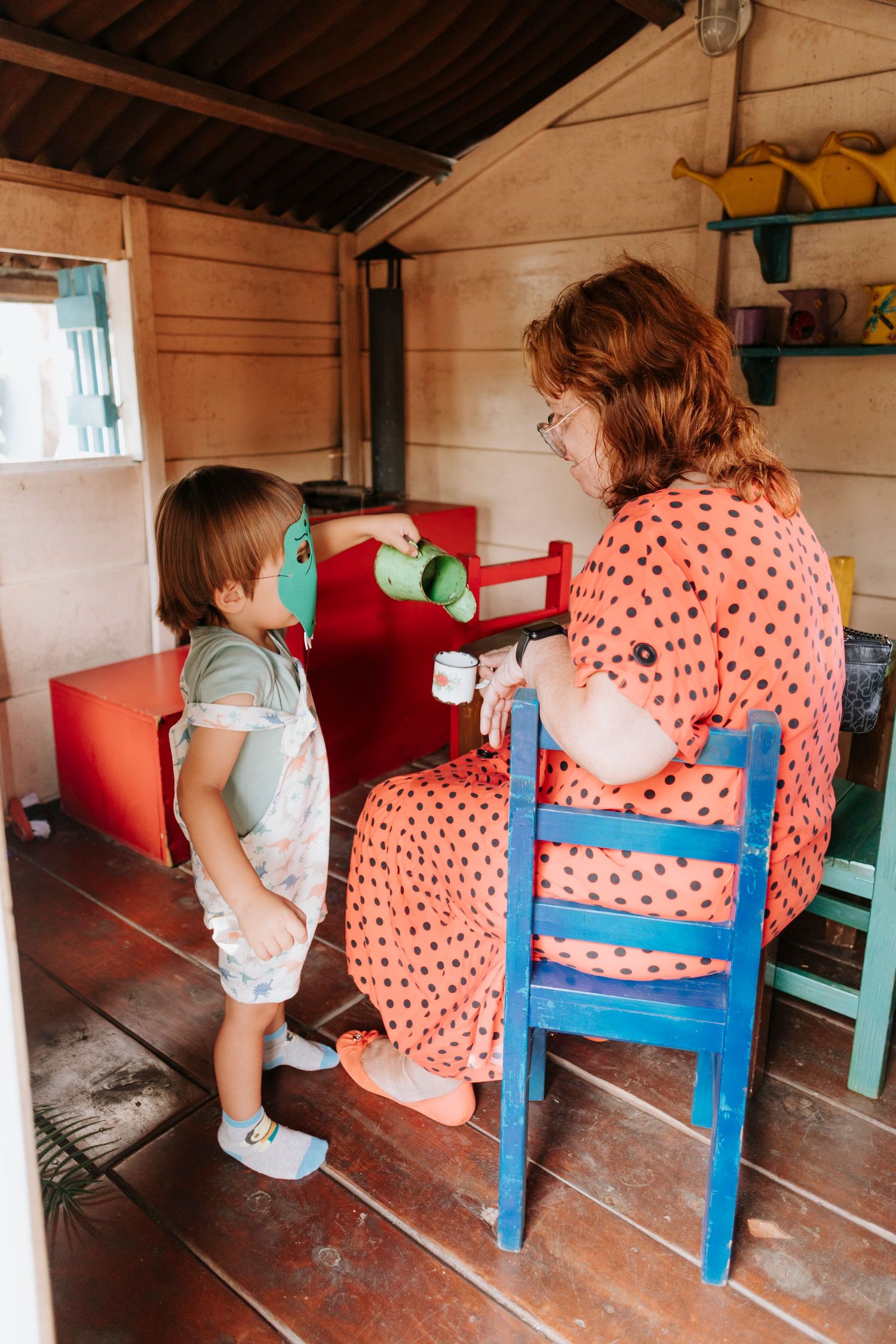 Parent and child playing together in wooden playhouse with dinosaur masks.