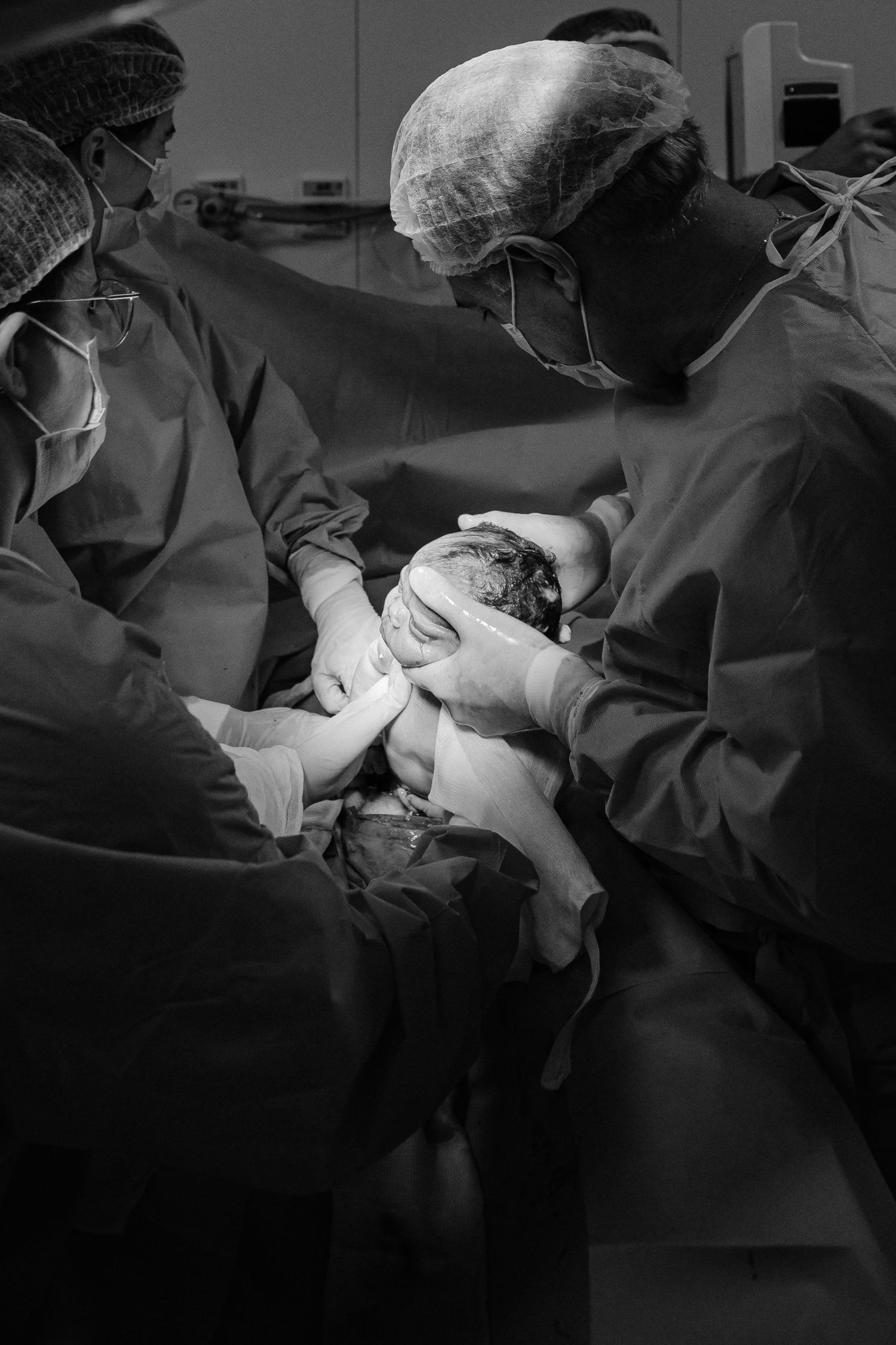 Medical staff in surgical attire assist during a childbirth procedure.