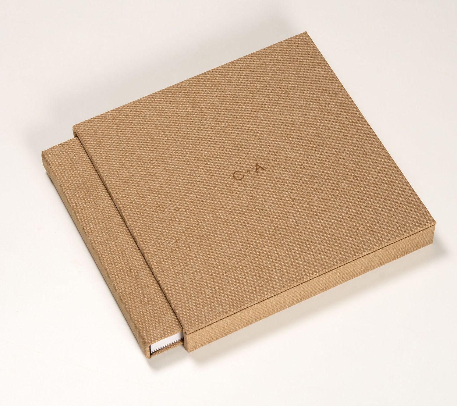 Kraft brown cardboard photo book with matching slip case, embossed with initials C and A, on white background.