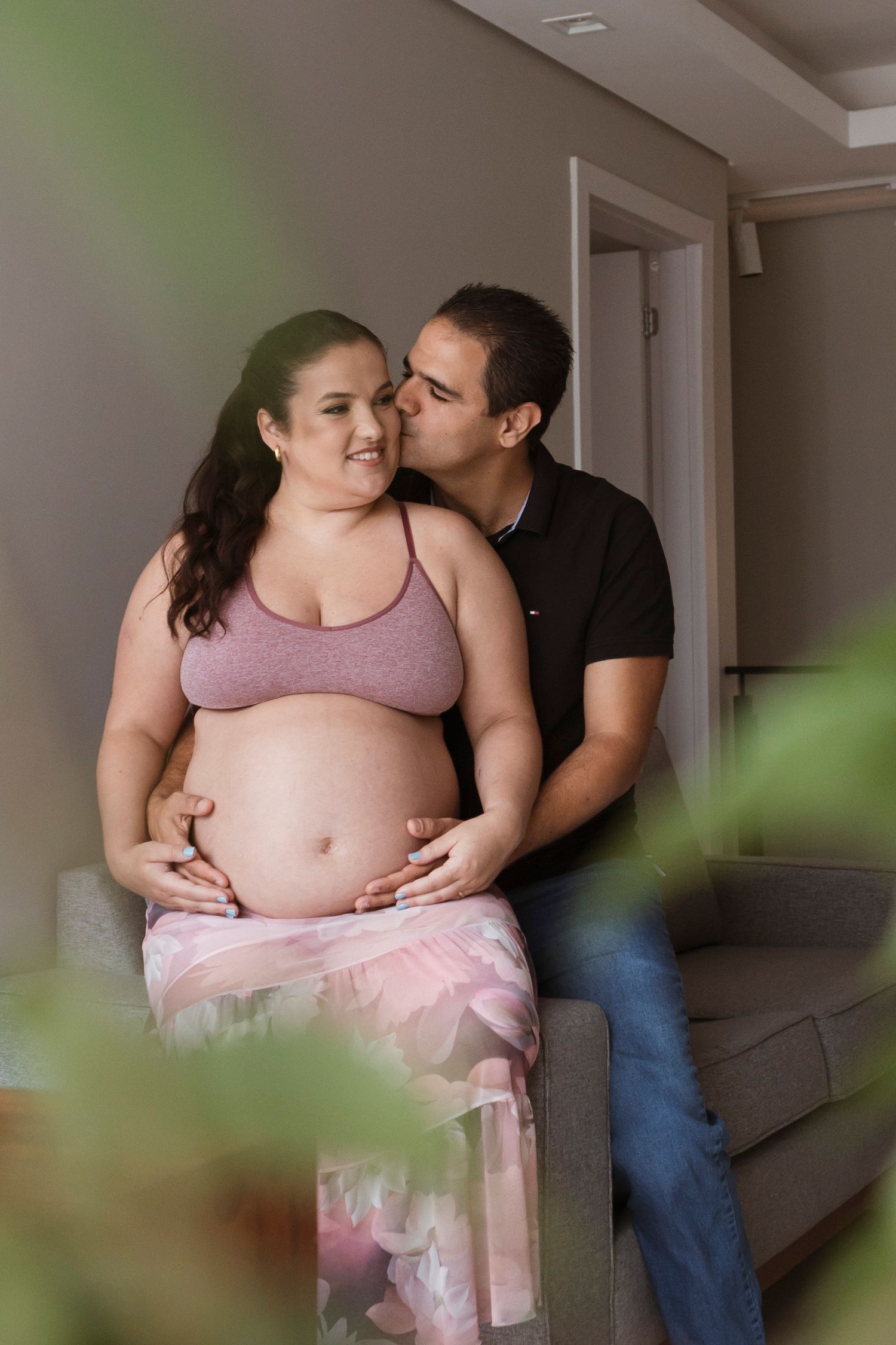Intimate maternity photo session showing tender moments between expecting couple in a softly lit indoor setting.