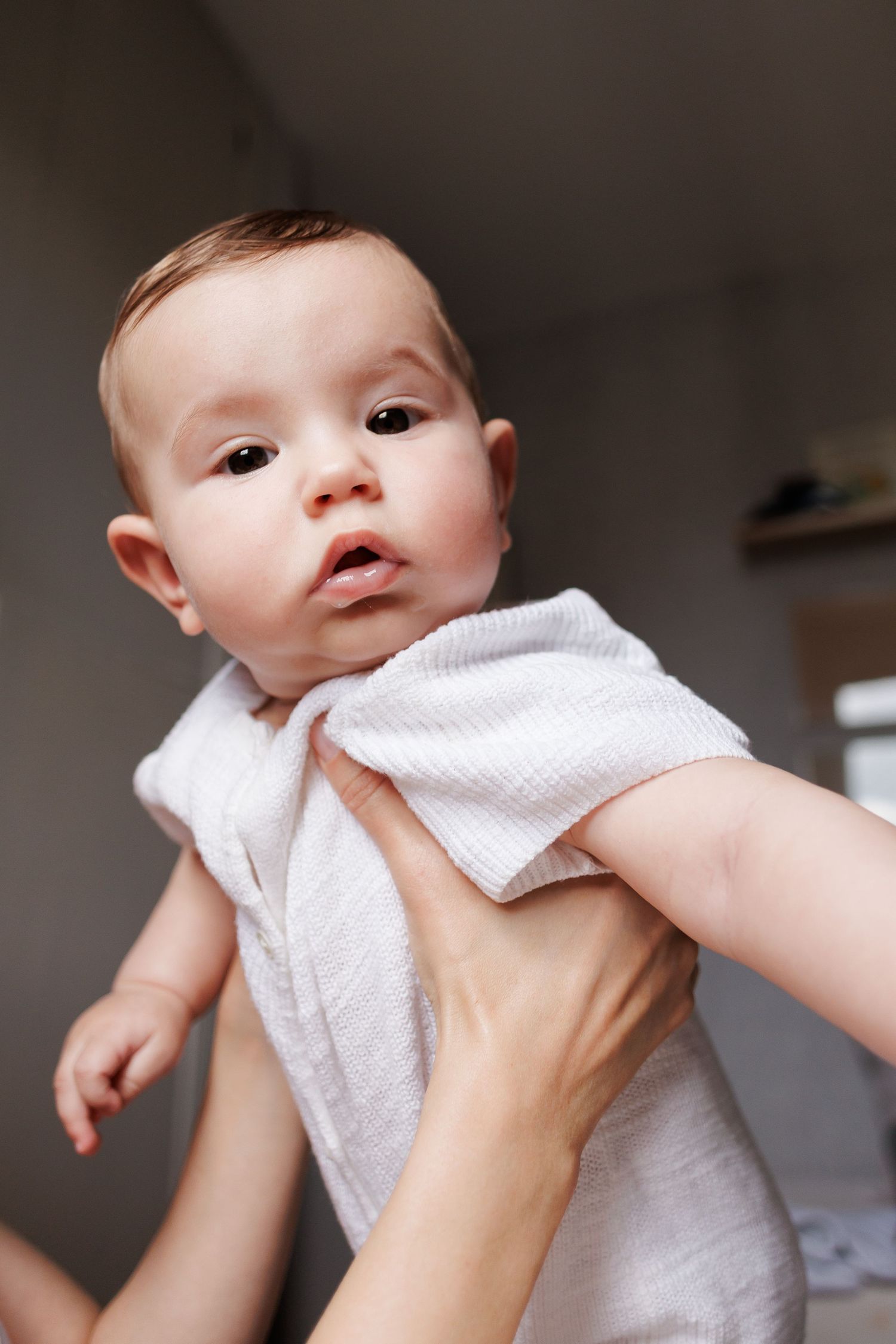 A baby wrapped in a white towel being held up by adult hands after bath time.