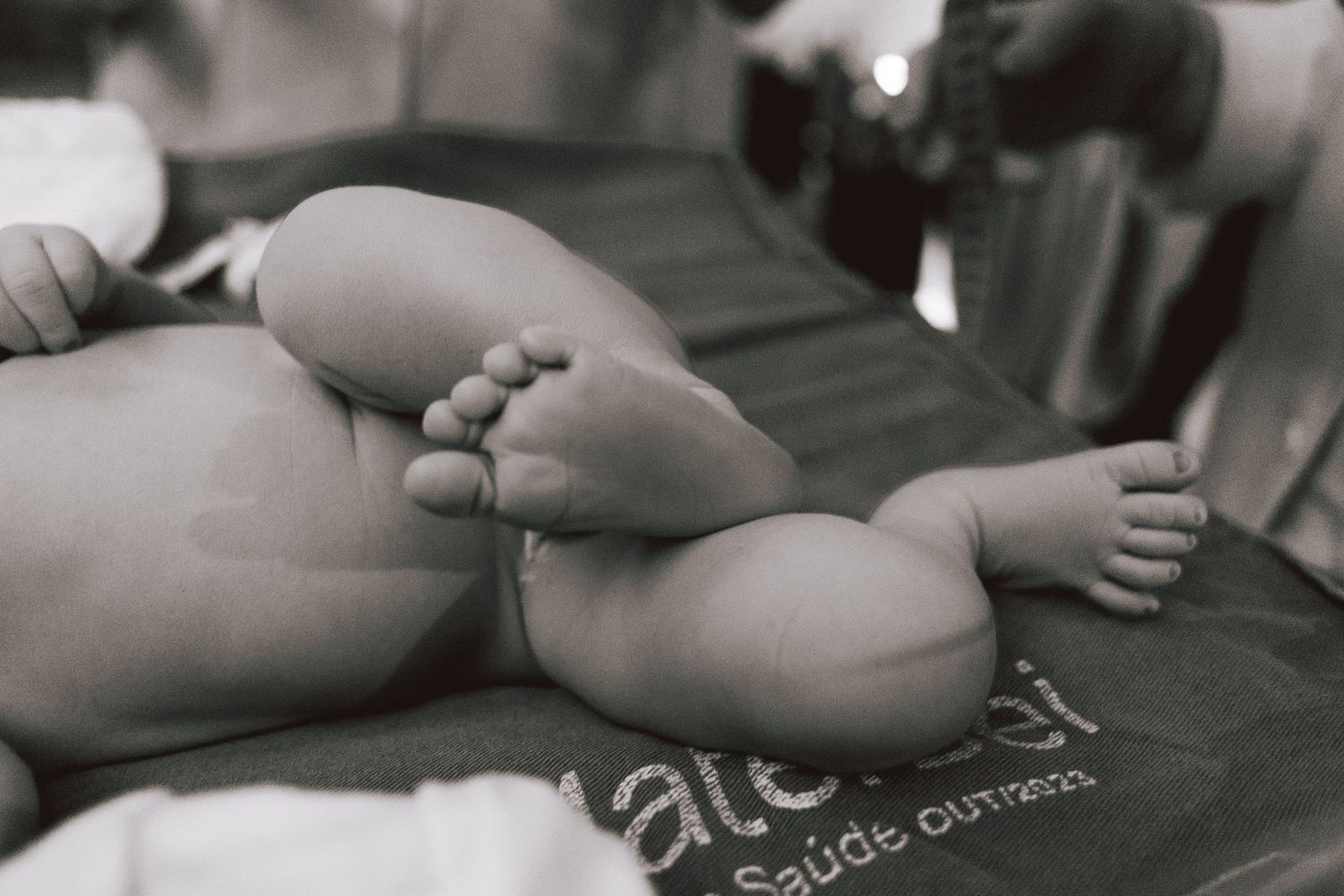 Black and white close-up photo of a newborn baby's tiny feet and legs resting on a surface.